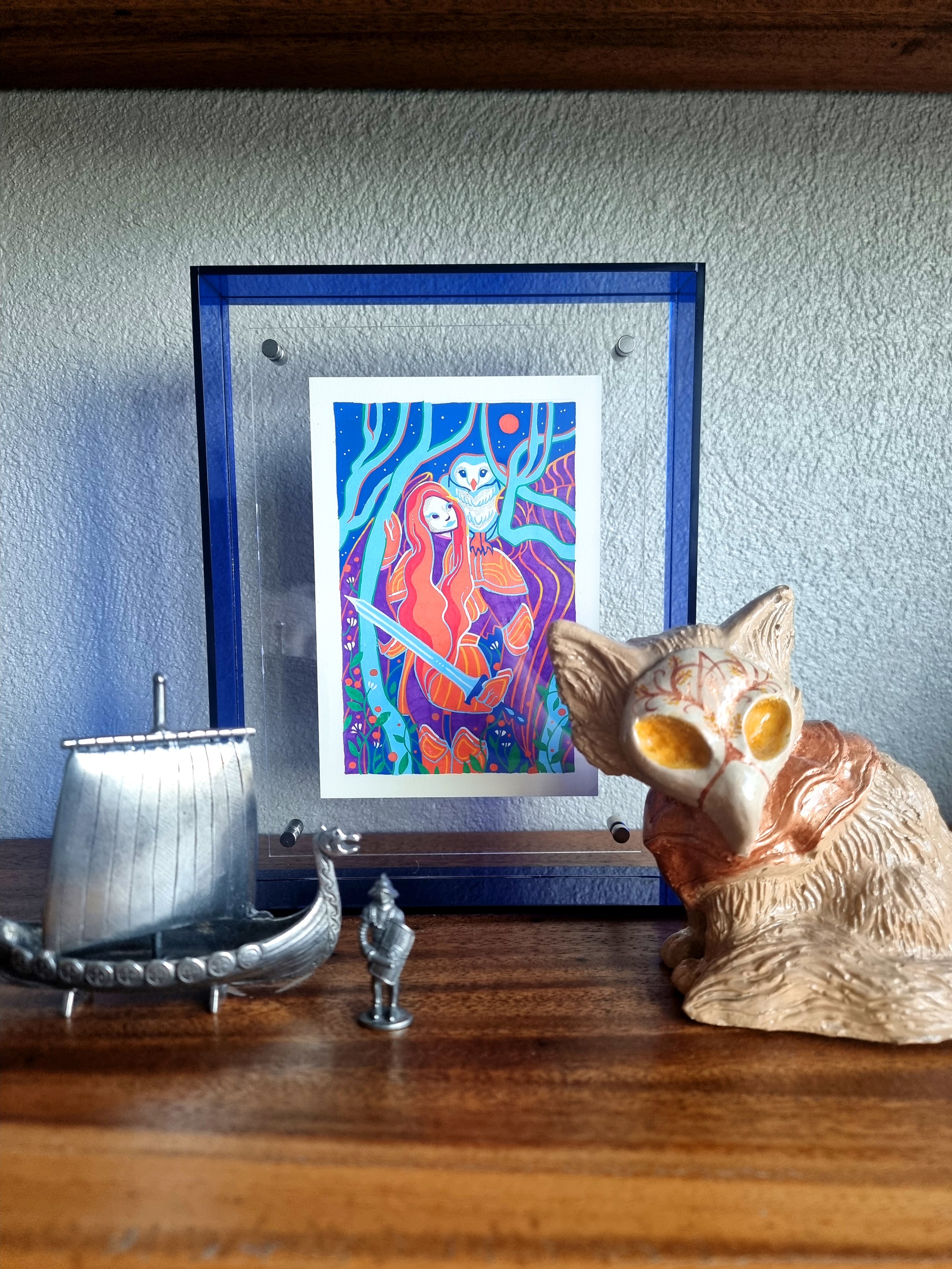 Decorative display shelf with a colorful fantasy-themed illustration, a silver Viking ship model, and a ceramic dog bust. The illustration features an owl, a wolf, and a sword amidst vibrant blue, orange, and purple colors. The shelf is made of wood with a textured wall background.