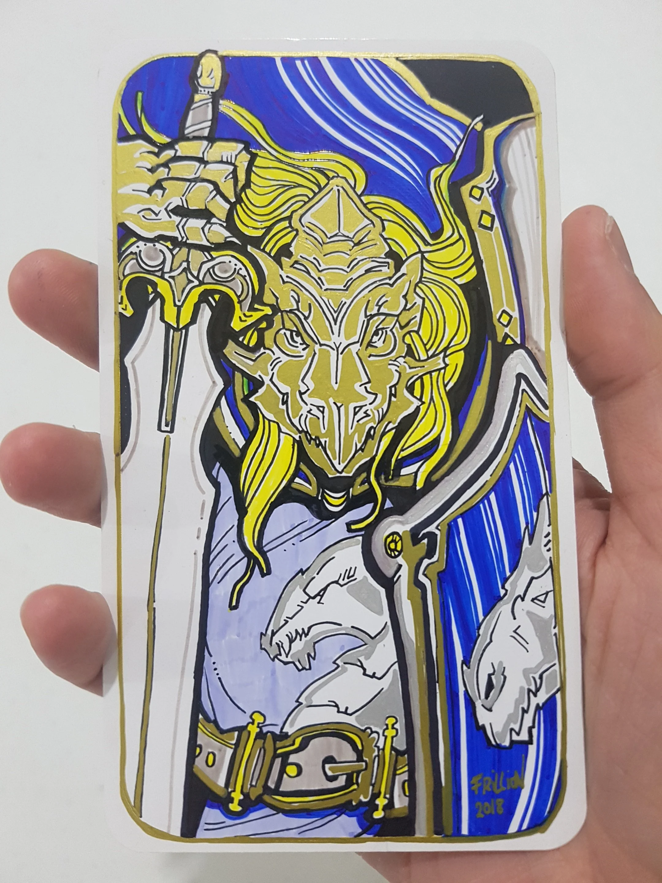 A sticker of a stylized dragon with gold, black, blue, and white colors, featuring intricate line work and details, held between fingers.