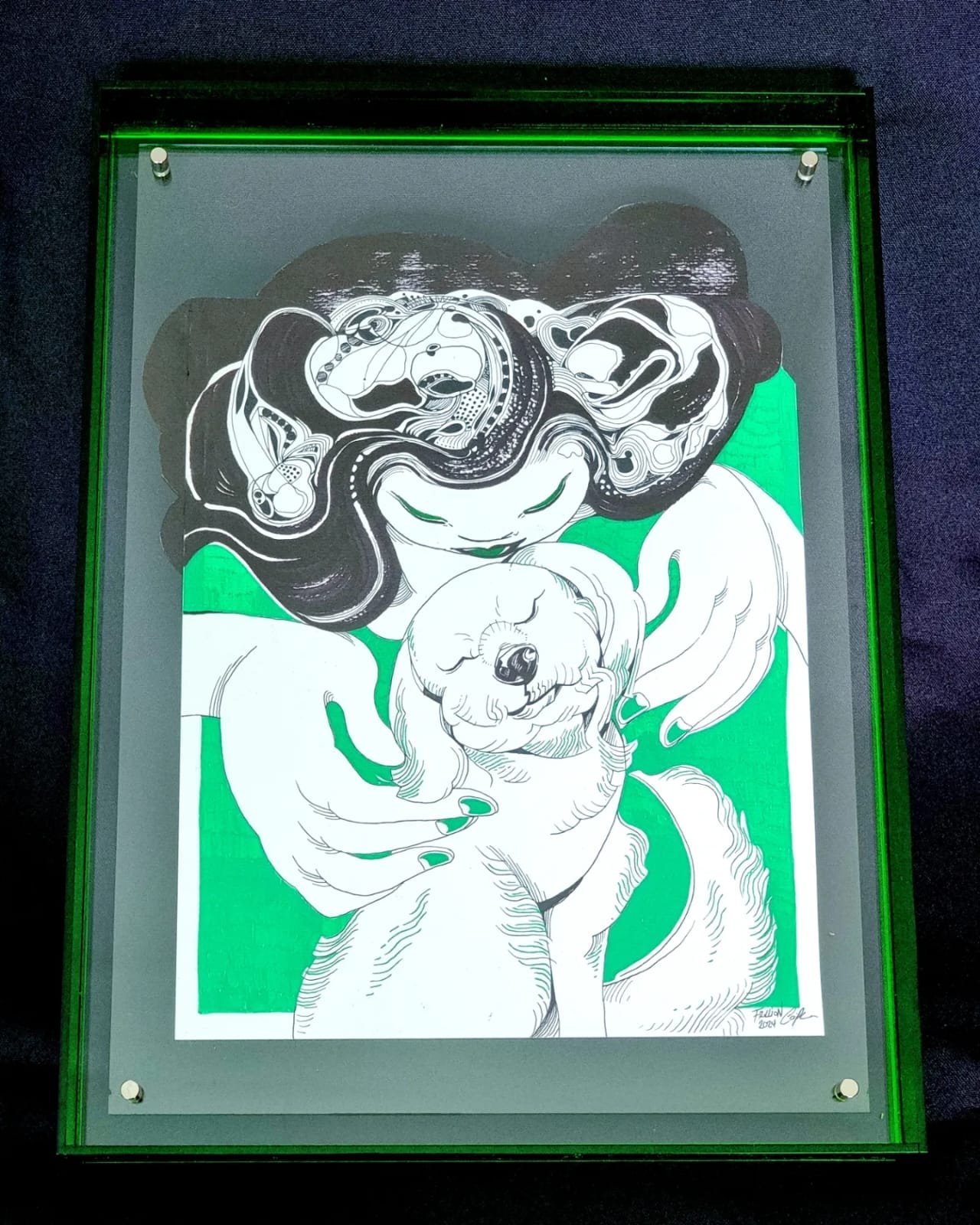 An illustration of a woman with long hair holding a small dog, with another dog partially visible at the bottom. The drawing uses black, white, and green colors, and is displayed under a glass frame with green lighting.