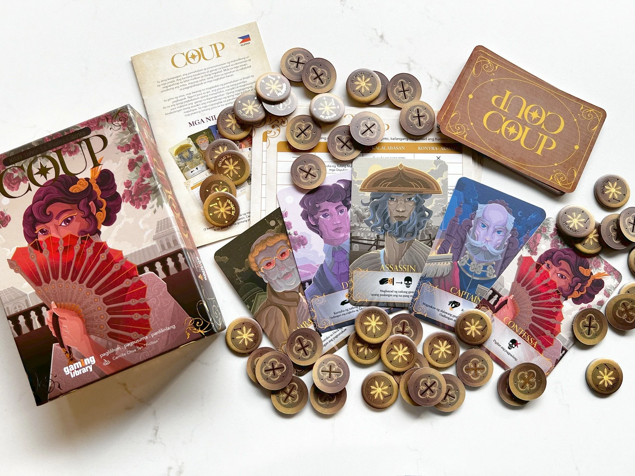 A collection of game pieces, cards, and instruction sheets from the board game 'Coup', displayed on a white surface.