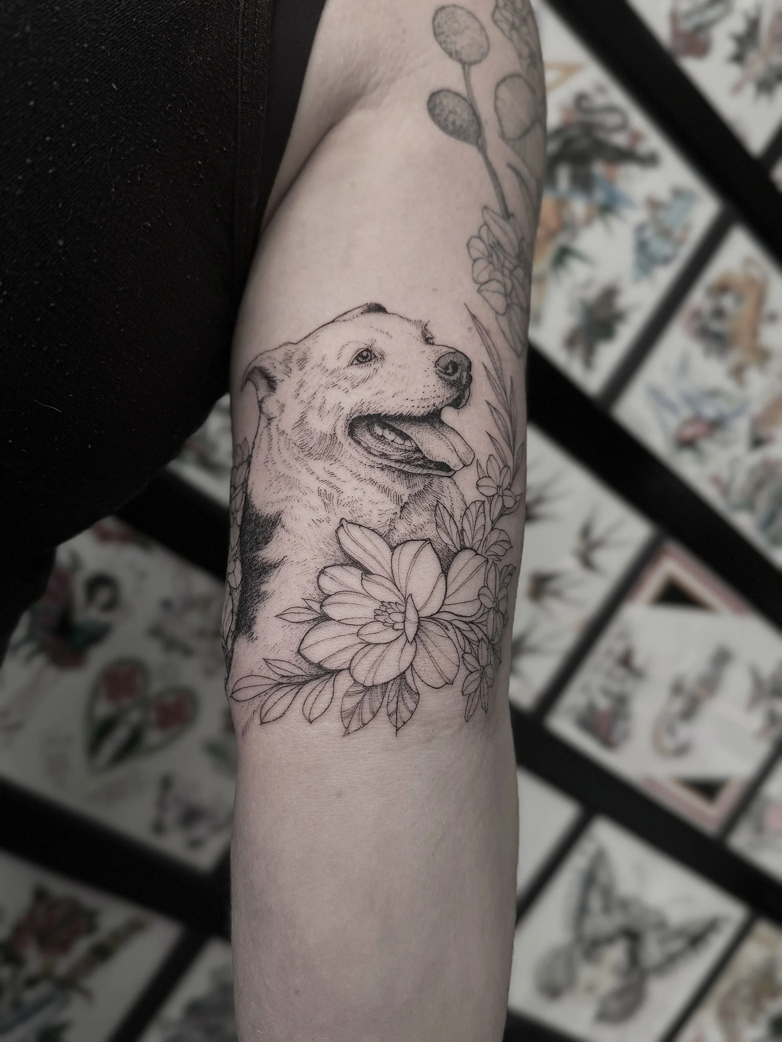 Black and white tattoo of a dog's head surrounded by flowers on a person's arm.