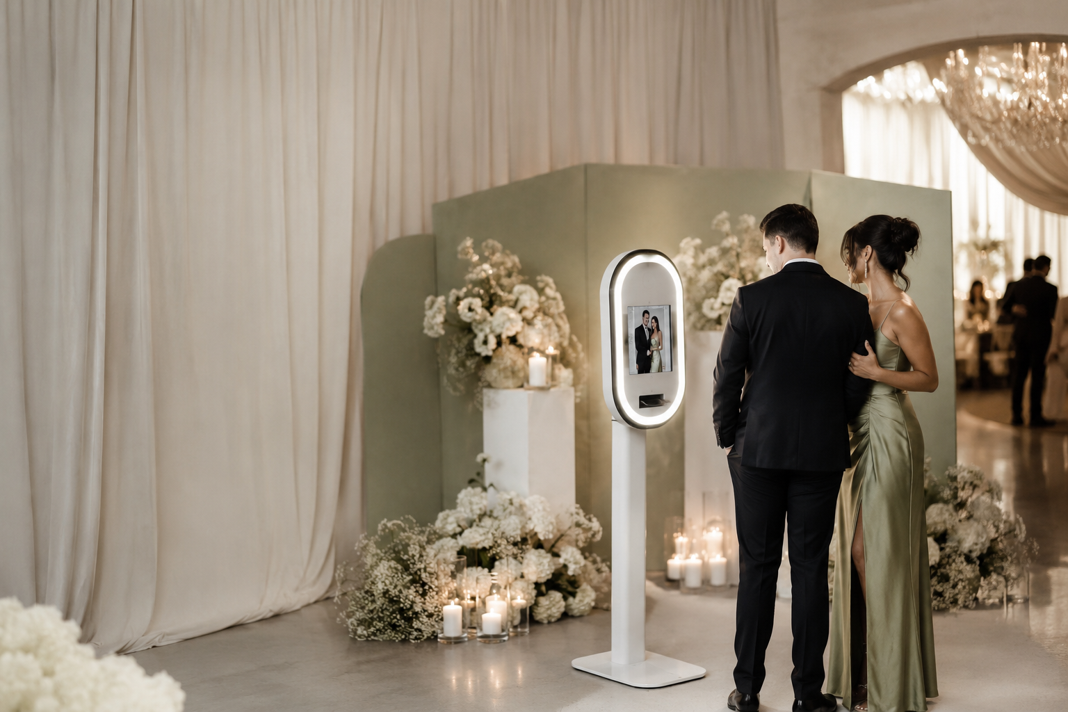 A couple in formal attire standing at a photo booth with floral arrangements and candles during a wedding reception.