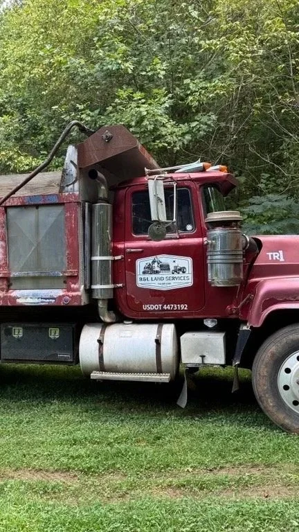 Red work truck with a logo for RSL Land Services parked on grass, surrounded by trees.