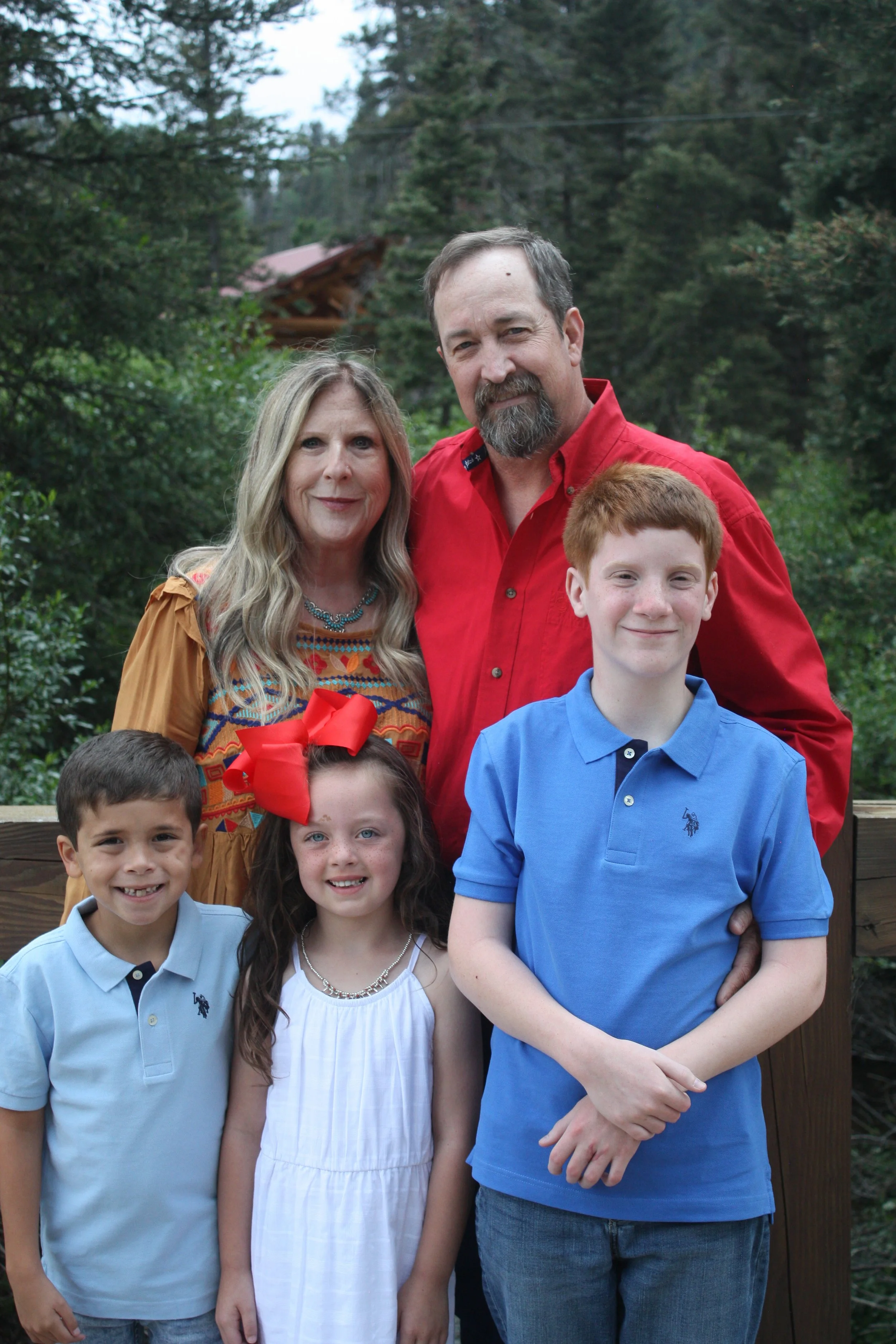 Family photo outdoors with two adults and four children, trees in background.