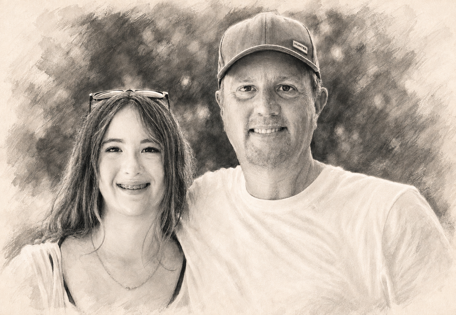 A smiling young woman with sunglasses on her head and a man wearing a baseball cap, both posing outdoors with bushes or trees in the background.