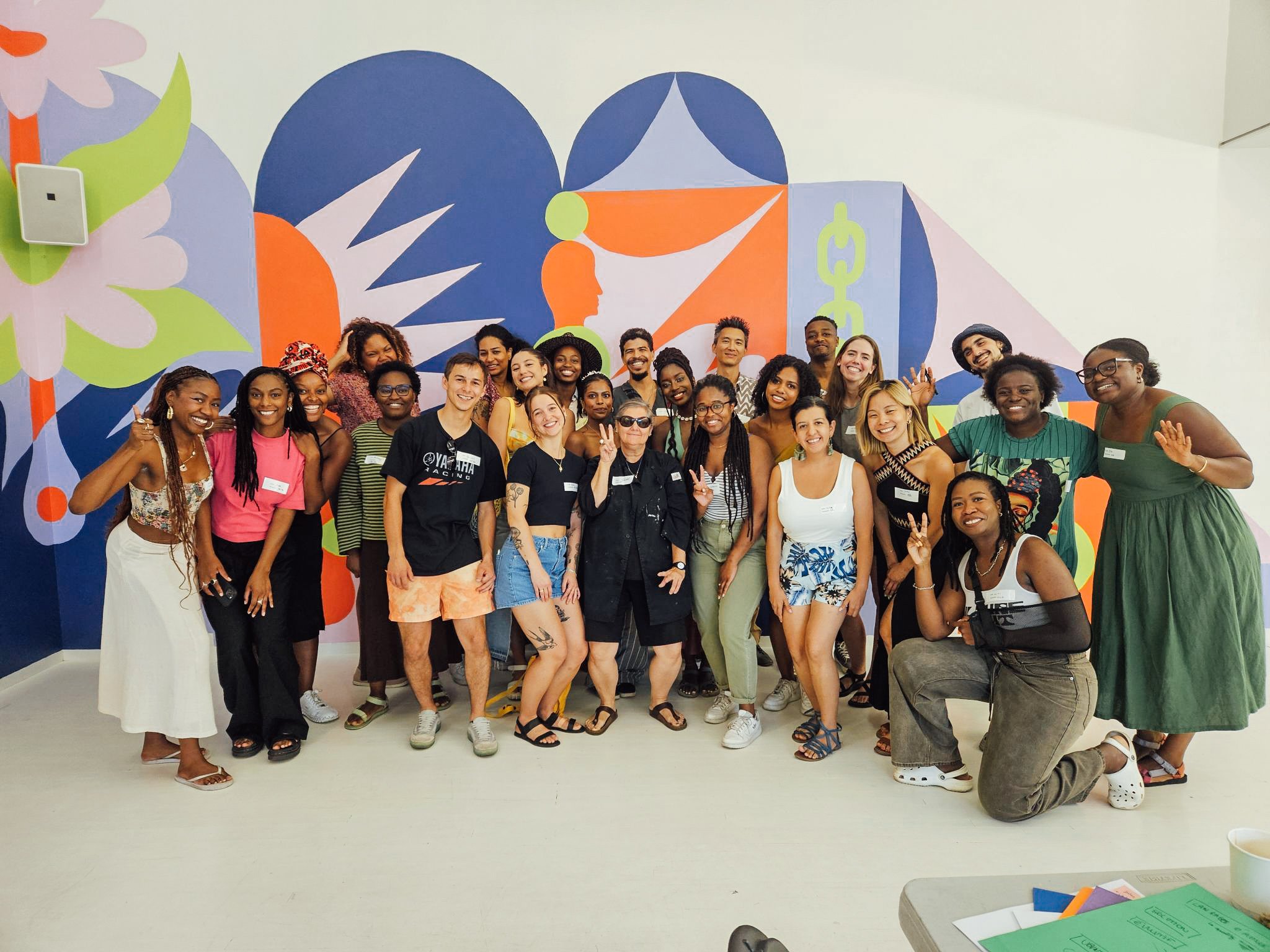 Groupe de personnes multiculturelles posant ensemble devant une fresque abstraite colorée.