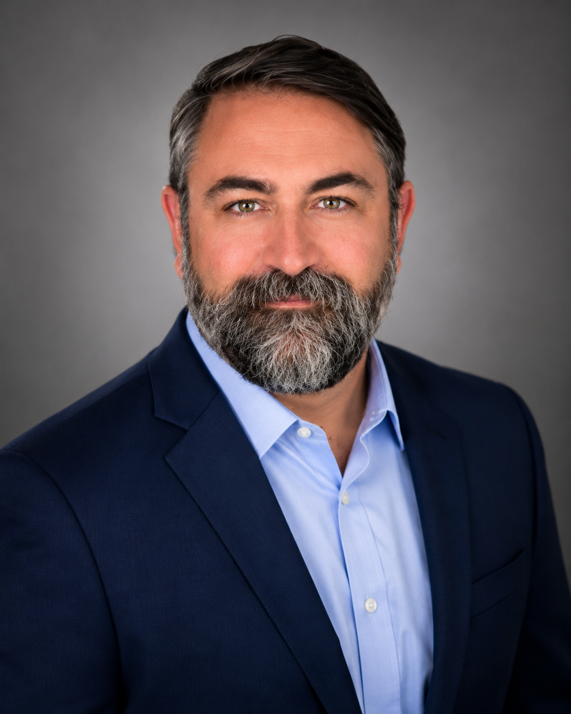 Man with blue shirt and navy jacket in front of grey background