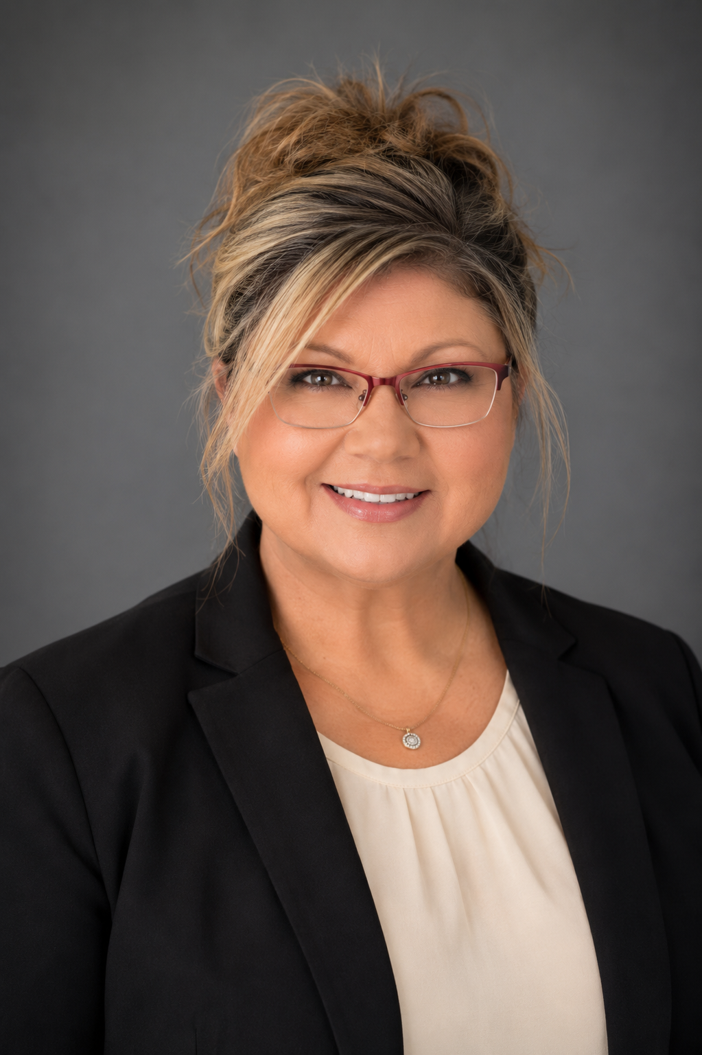 woman with glasses wearing tan shirt and black jacket in front of grey background
