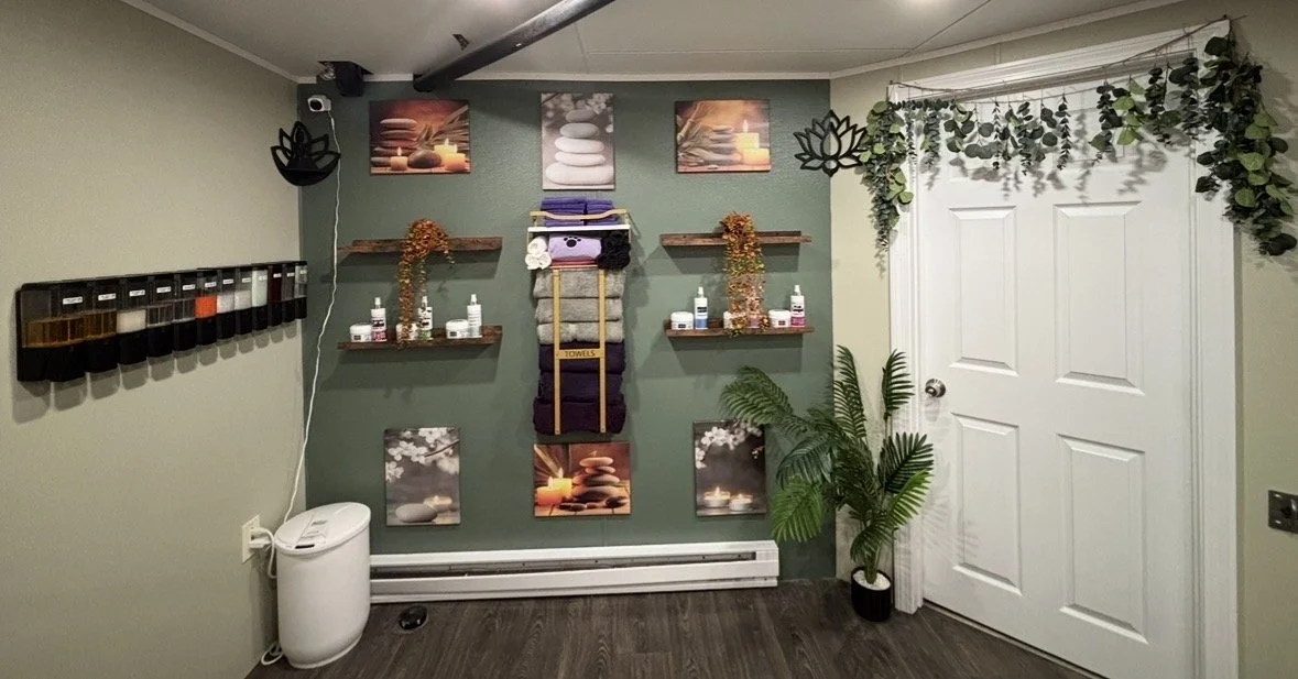 Spa or massage room with wall-mounted shelves, plants, towels, essential oils, and decorative pictures of stones and candles.