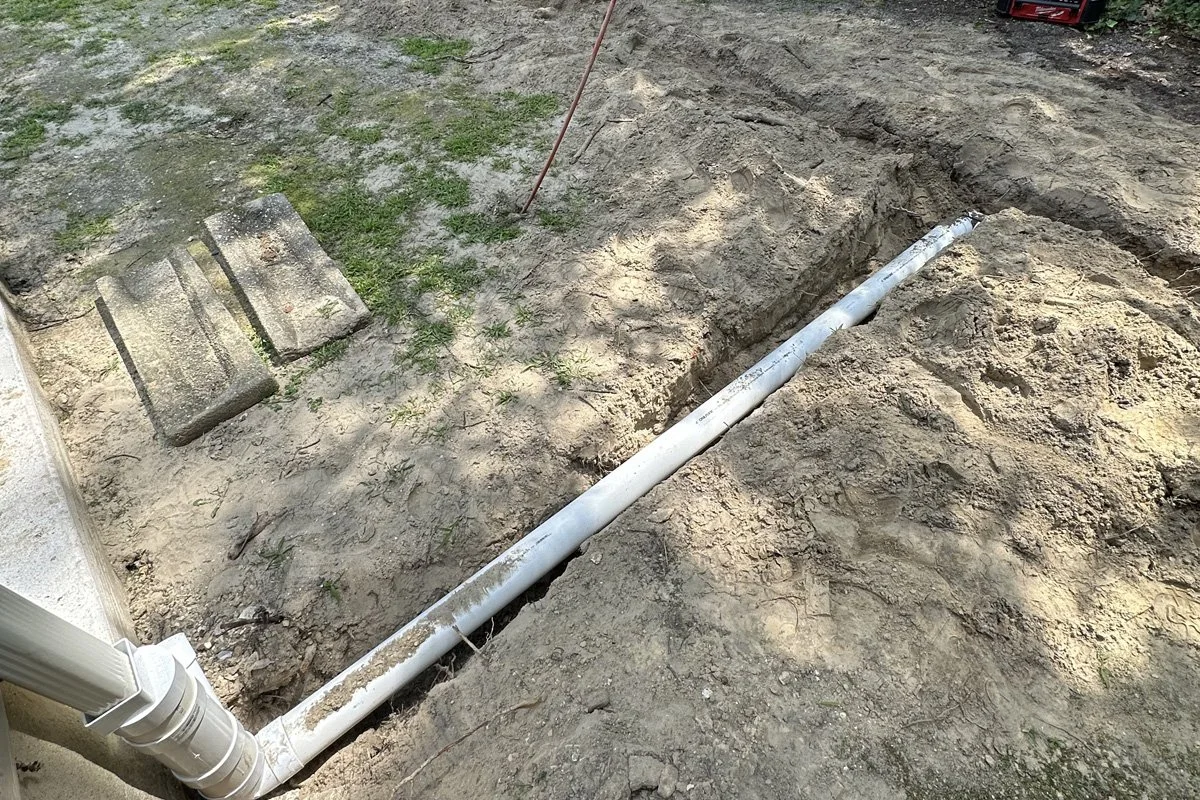 A white PVC underground gutter drain pipe connected to a home downspout inside an excavated trench to fix yard flooding in Washington Township, New Jersey.