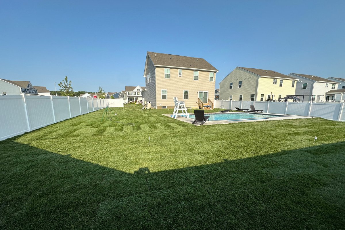 Wide-angle overview of a large backyard showing corrected grading and fresh topsoil preparation before laying new sod around an in-ground pool.