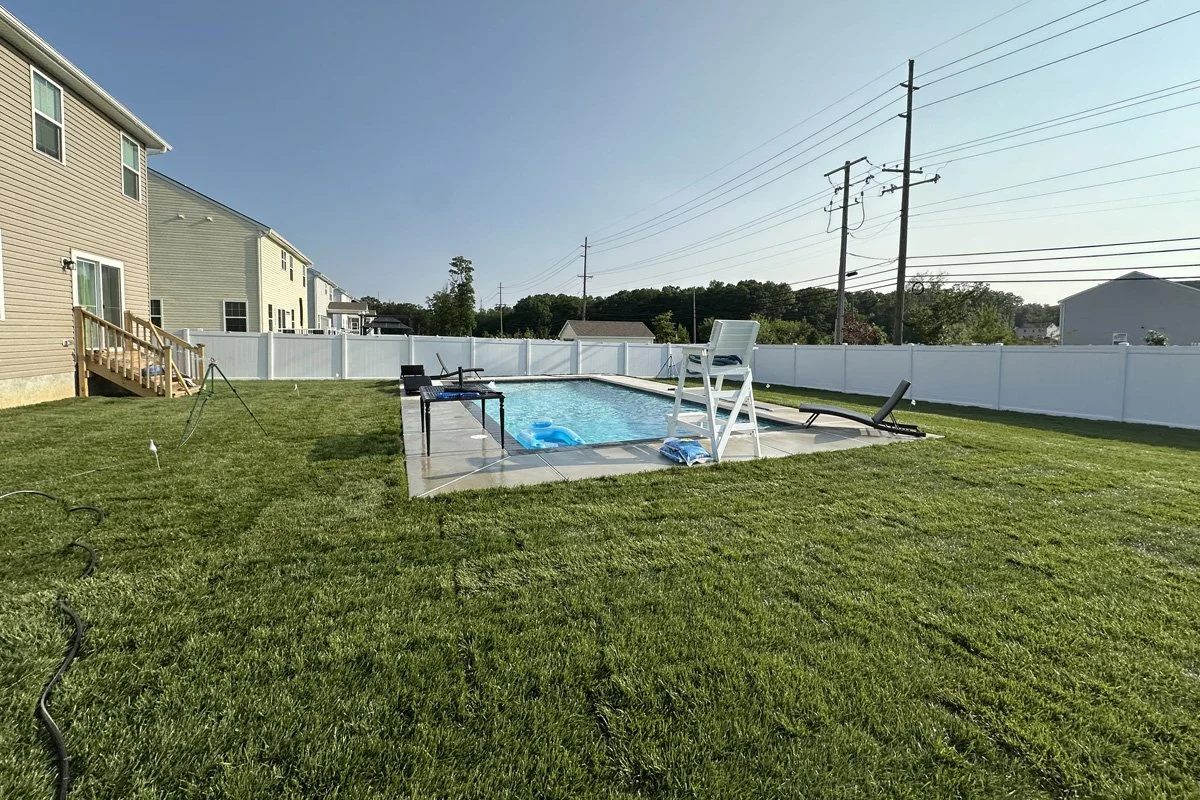View towards the pool showcasing fresh-cut lawn sod meeting seamlessly with the concrete patio and backyard stairs.