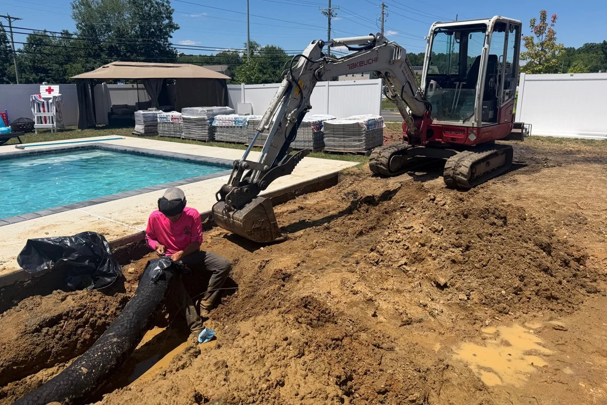 Hardscaping contractor laying perforated French drain pipe with mini excavator for backyard water management in Monroe Township.