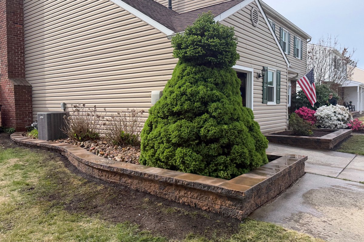 Side yard retaining wall enclosing a landscaped bed and evergreen tree using Cambridge Matrix Toffee Onyx stone blocks in Sewell.
