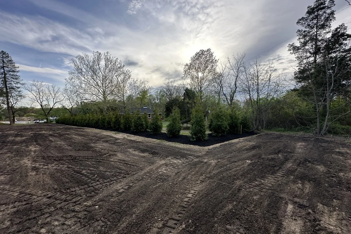 Wide-angle perspective of an extensive property line installation in Gloucester Township, NJ, featuring a large L-shaped row of newly planted arborvitae privacy trees set in rich black mulch beds with freshly graded topsoil.
