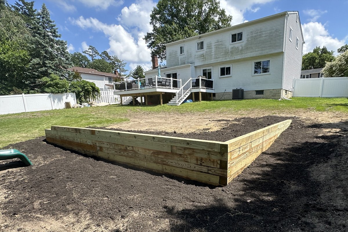 A massive, newly constructed wood timber retaining wall built to level a heavily sloped residential backyard with fresh topsoil ready for seeding.