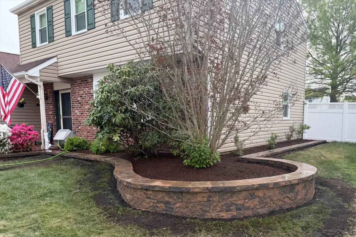 Detailed view of a custom 175-linear-foot curved garden retaining wall with dark brown mulch and fresh plantings in Sewell, NJ.