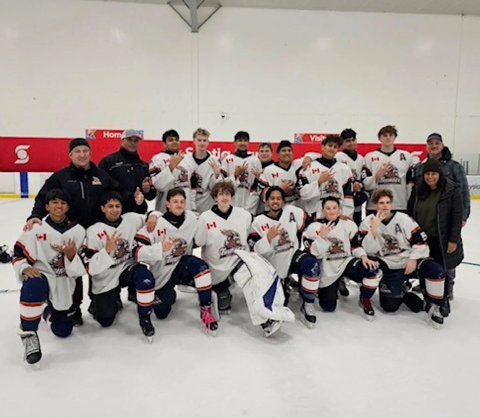 A youth hockey team posing for a group photo on ice rink with coaches, all wearing white jerseys with Canadian flags and a bear logo.
