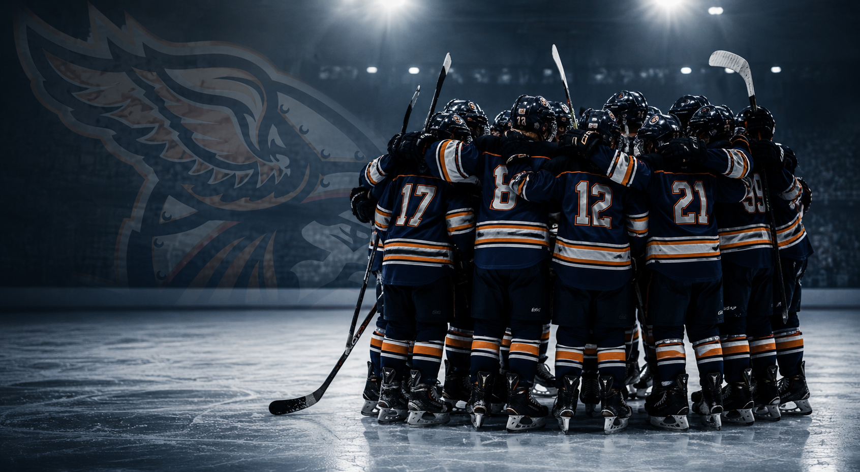 A hockey team in dark blue jerseys with orange and white stripes huddles together on the ice rink during a game or practice, with a large, transparent team logo in the background.