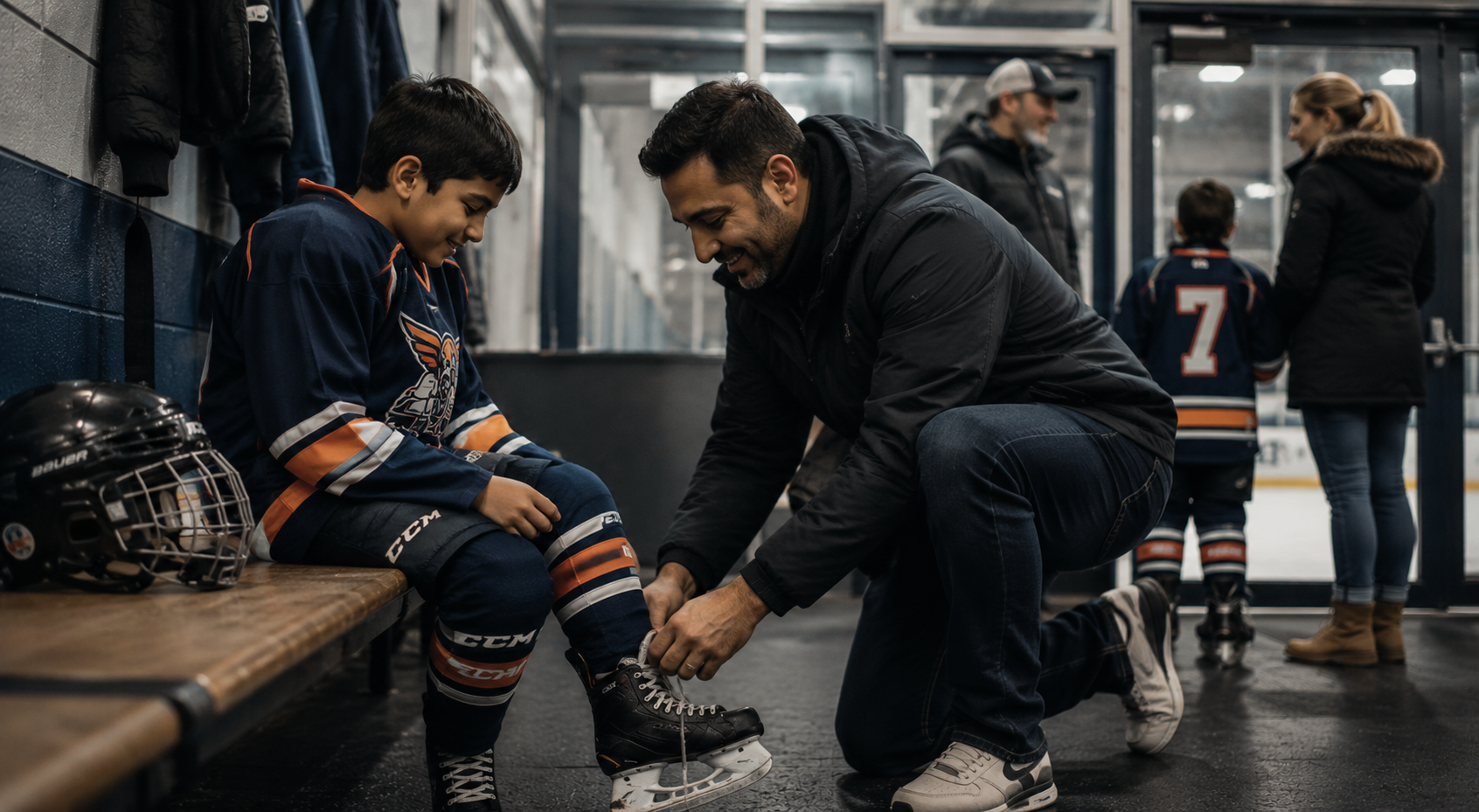 A father kneeling on the ice rink tying his son's hockey skates, with hockey gear and a helmet nearby, while other families and a young player in hockey uniforms are in the background.