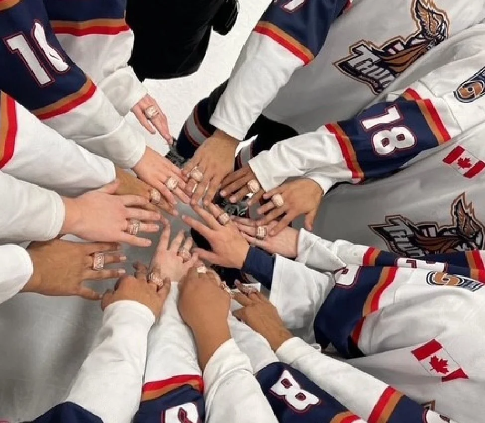 Group of people wearing hockey jerseys putting their hands together in a huddle.