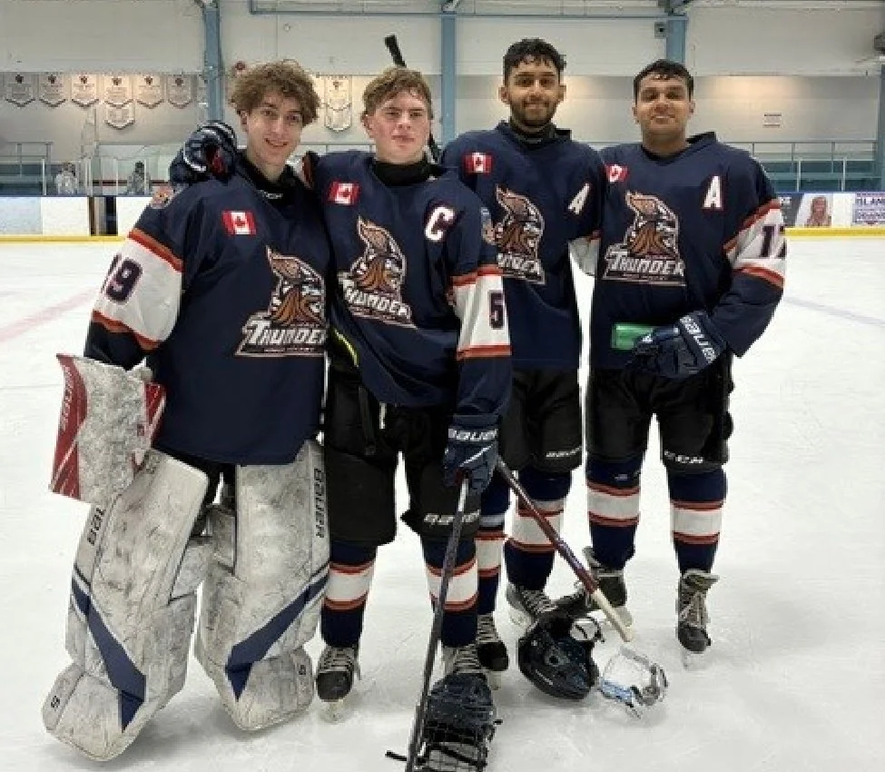 Four male ice hockey players in navy blue jerseys with 'Thunder' logo, standing on the ice rink, smiling, with one player in goalie gear.
