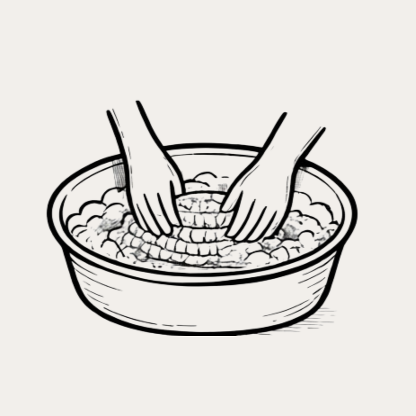 Two hands washing or scrubbing food in a large bowl of water.