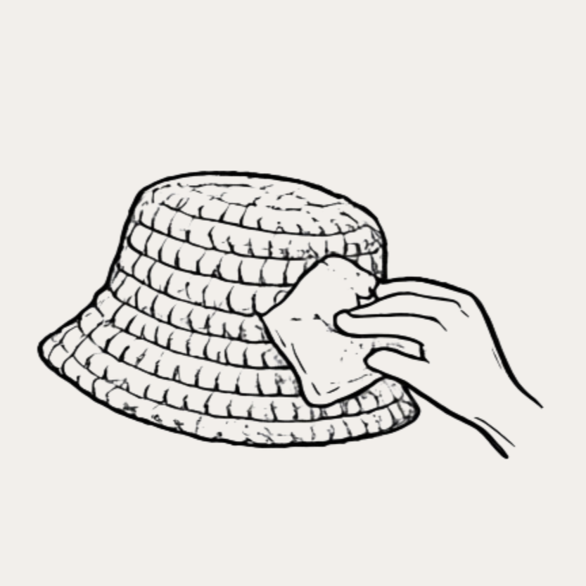 A hand cleaning a bucket hat with a cloth.