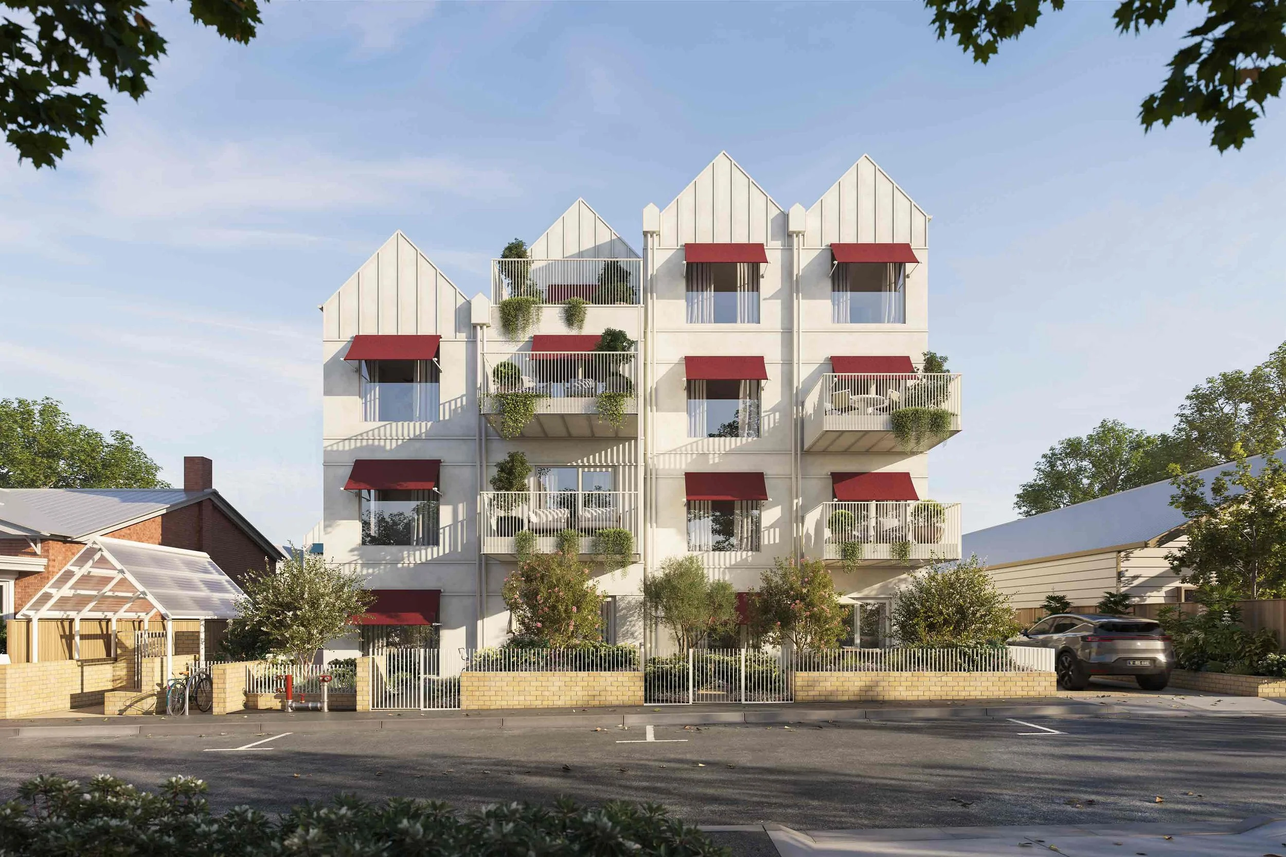A modern white apartment building with multiple balconies, some with red awnings and greenery, under a clear blue sky, with trees and parked cars in the foreground.