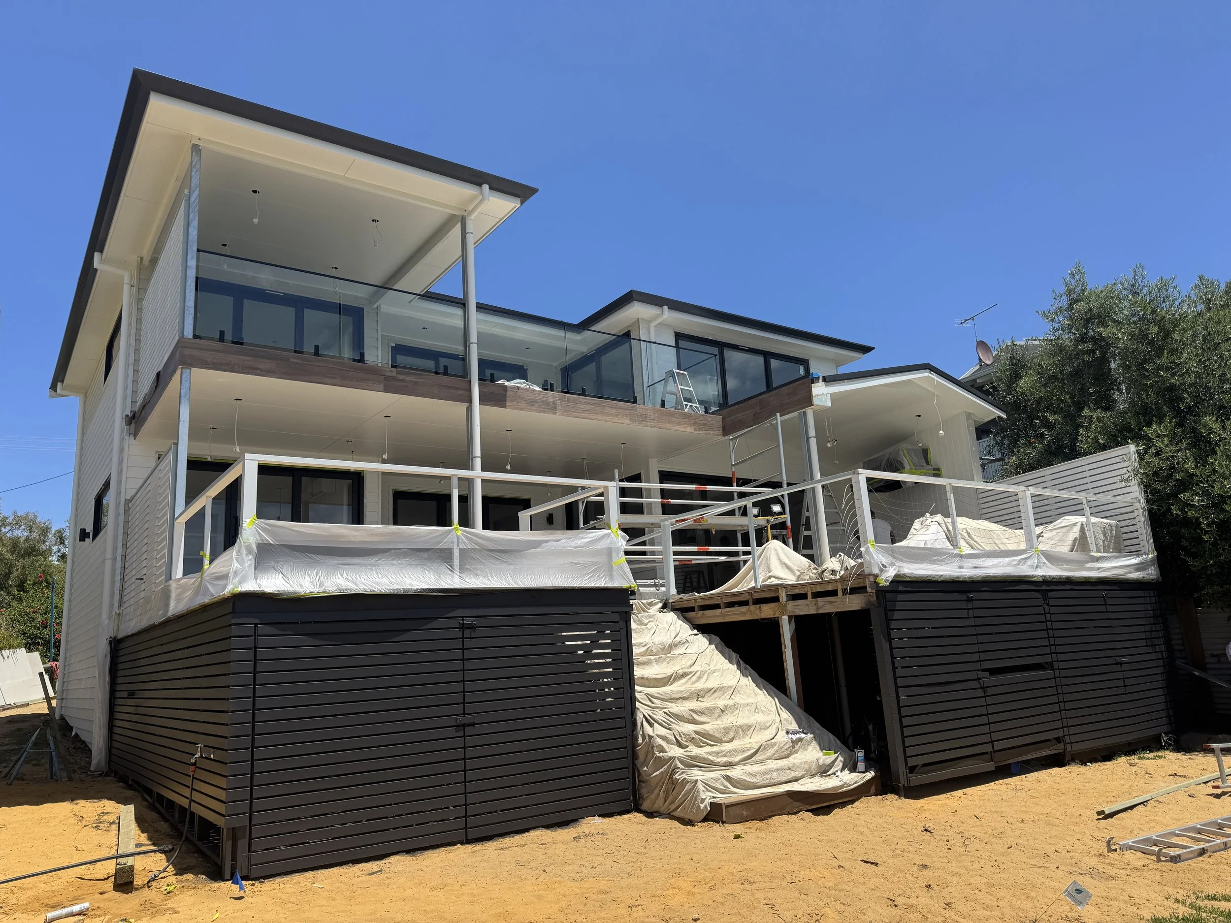 Under construction multi-story modern house with scaffolding, glass balconies, and a mix of black and white exterior materials.