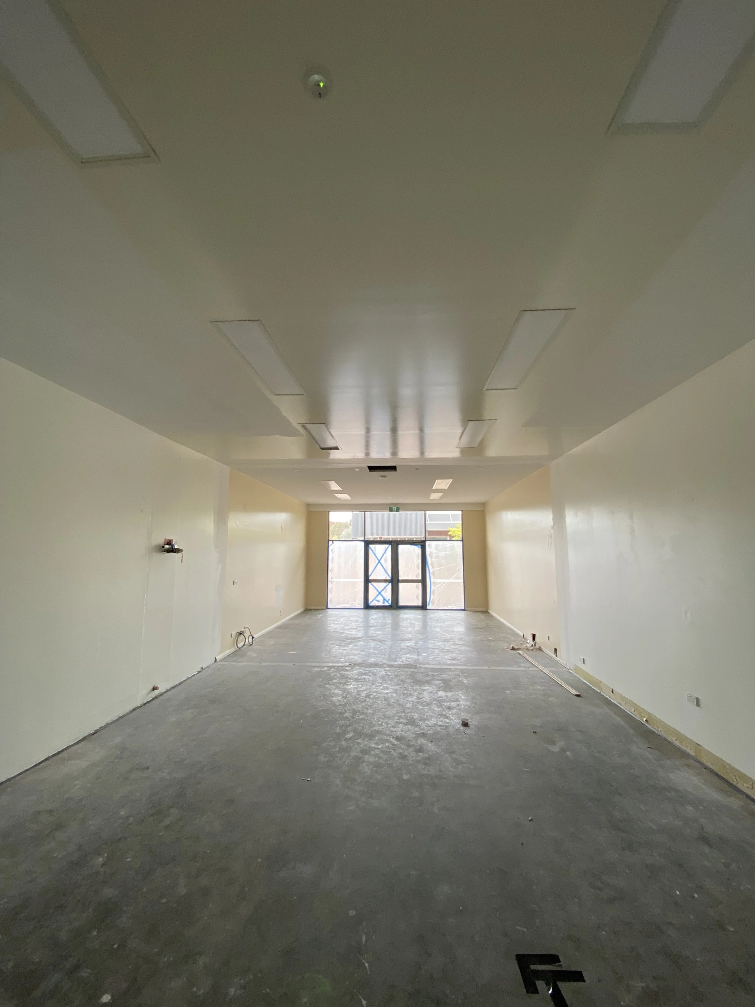 Empty room under construction with yellow walls, ceiling lights, and a large window at the end, with construction materials on the floor.