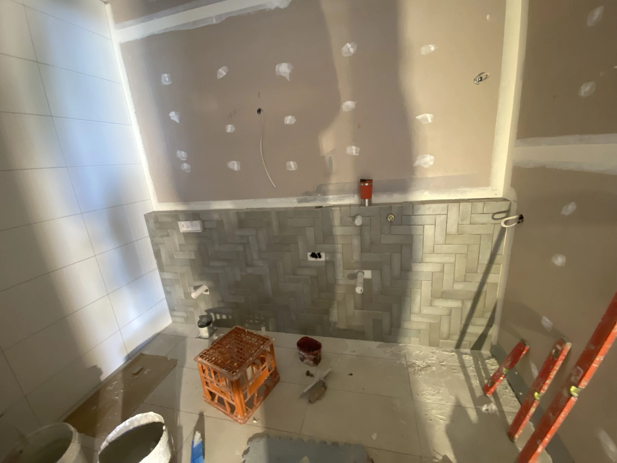 Construction site with missing drywall and electrical outlets in a partially finished room, with construction tools and materials scattered around.
