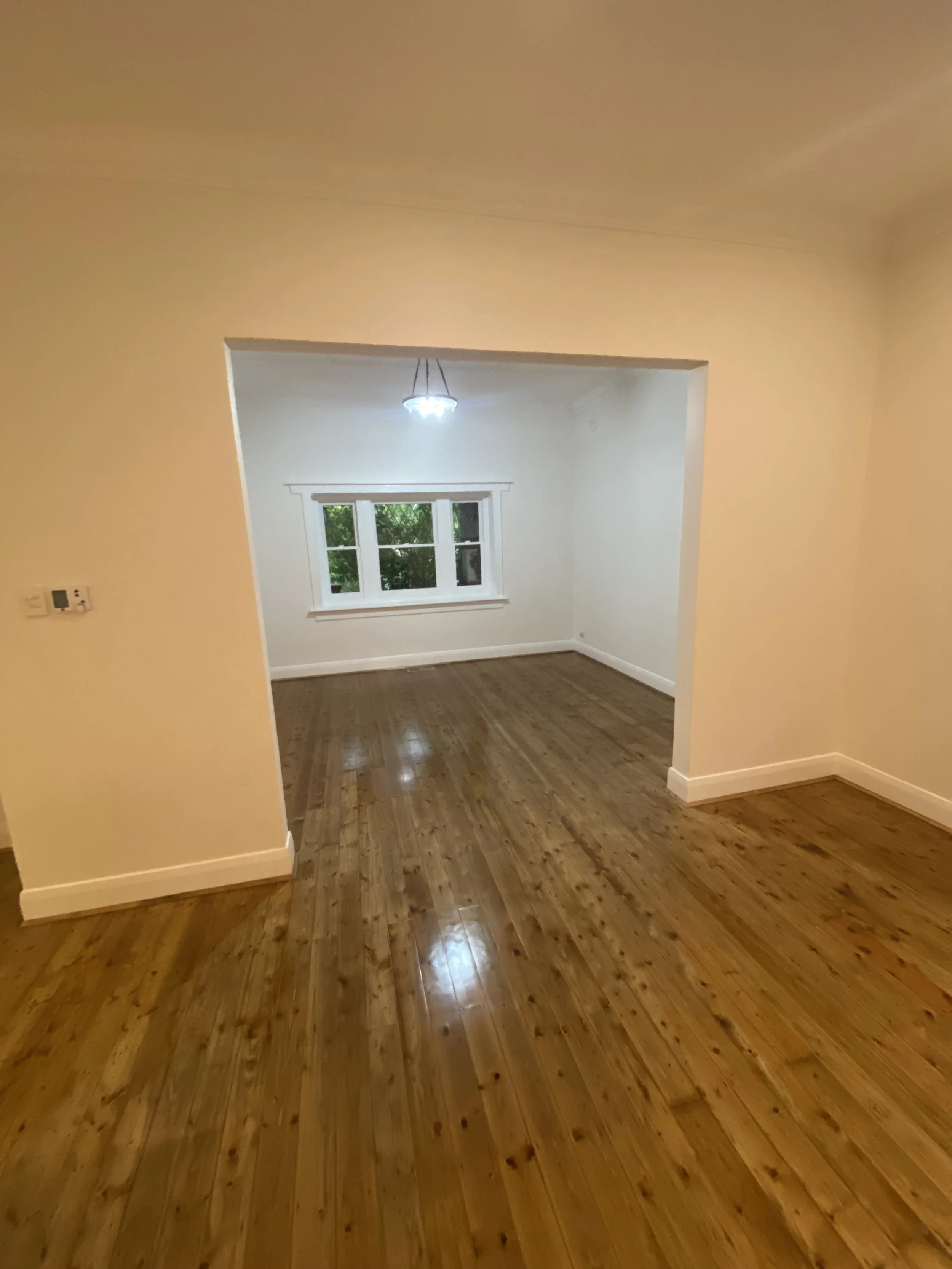 Room with hardwood floors, white walls, a window with multiple panes, and a ceiling light fixture.