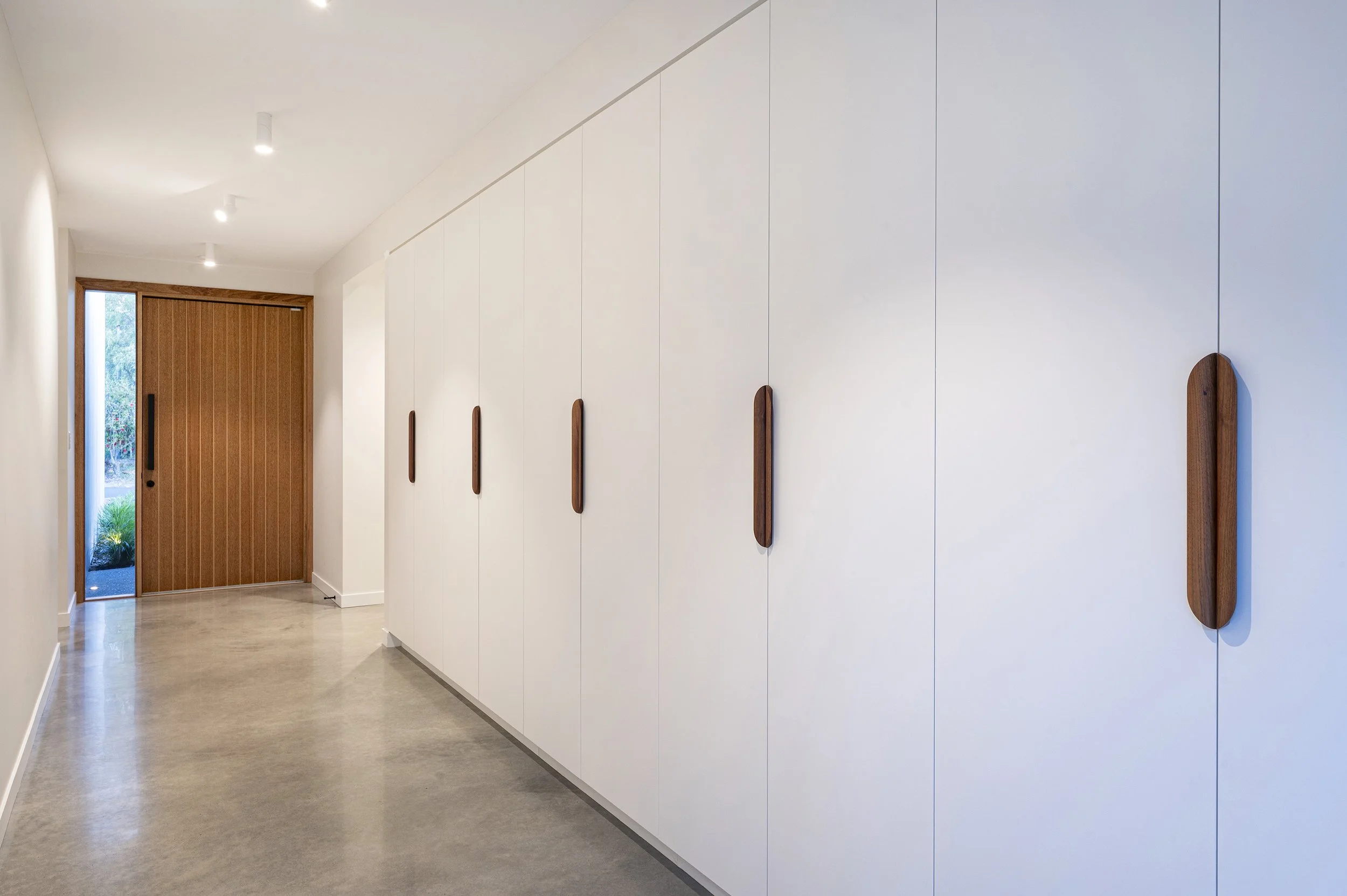 Modern interior hallway with white wall panels, wooden door, and minimalist wooden wall accents.