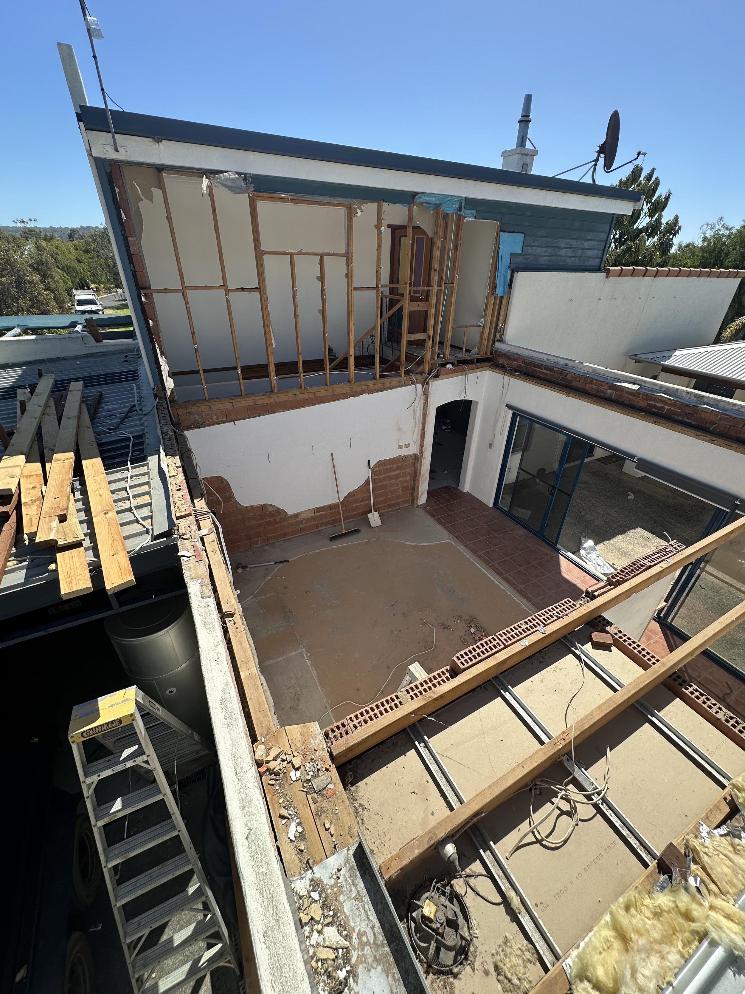 Side view of a building under renovation, showing exposed wooden framing, boat parts, and construction materials.