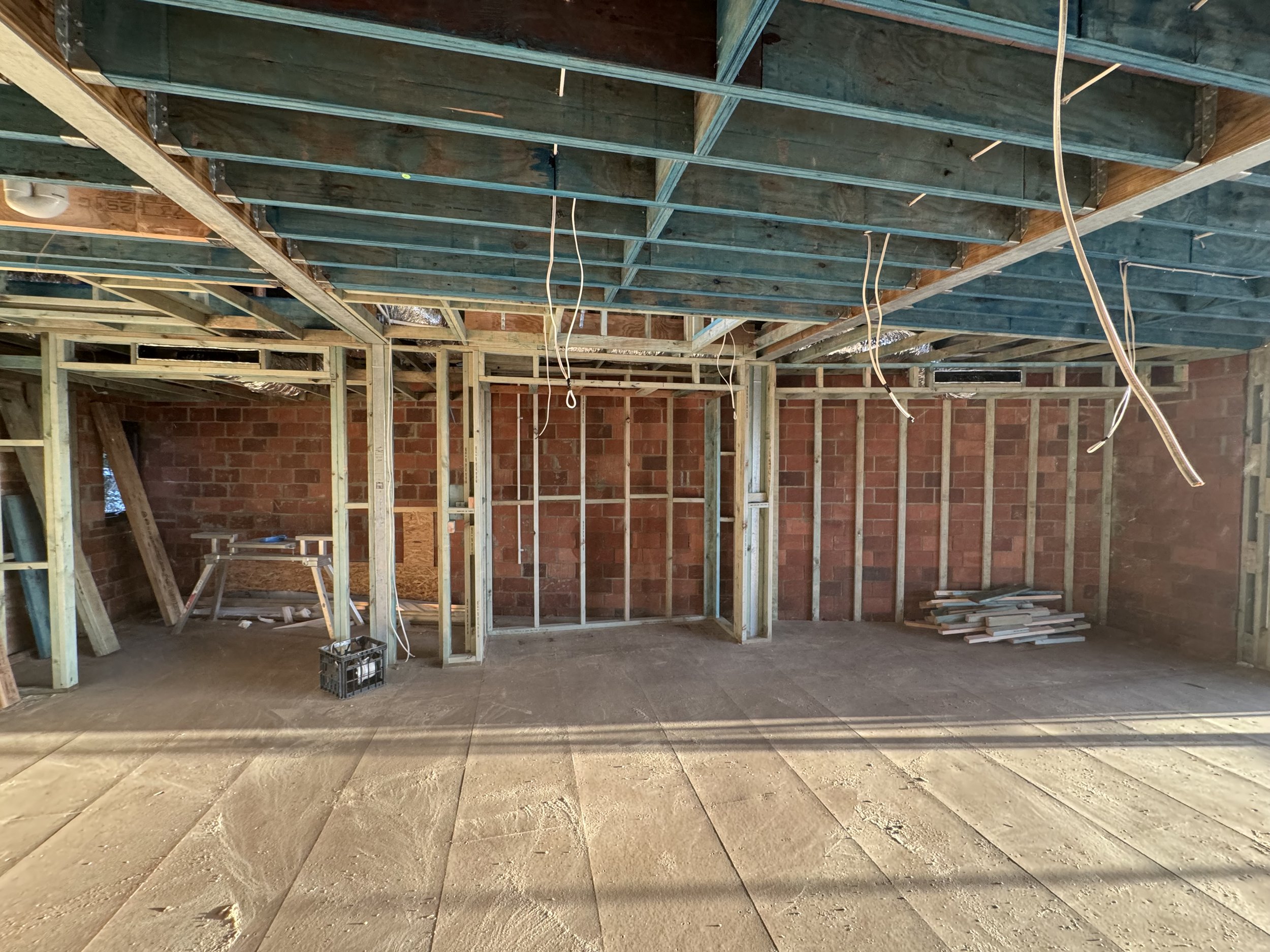 Interior of a building under construction with wooden framing, exposed electrical wiring, brick walls, and large stone floor tiles.