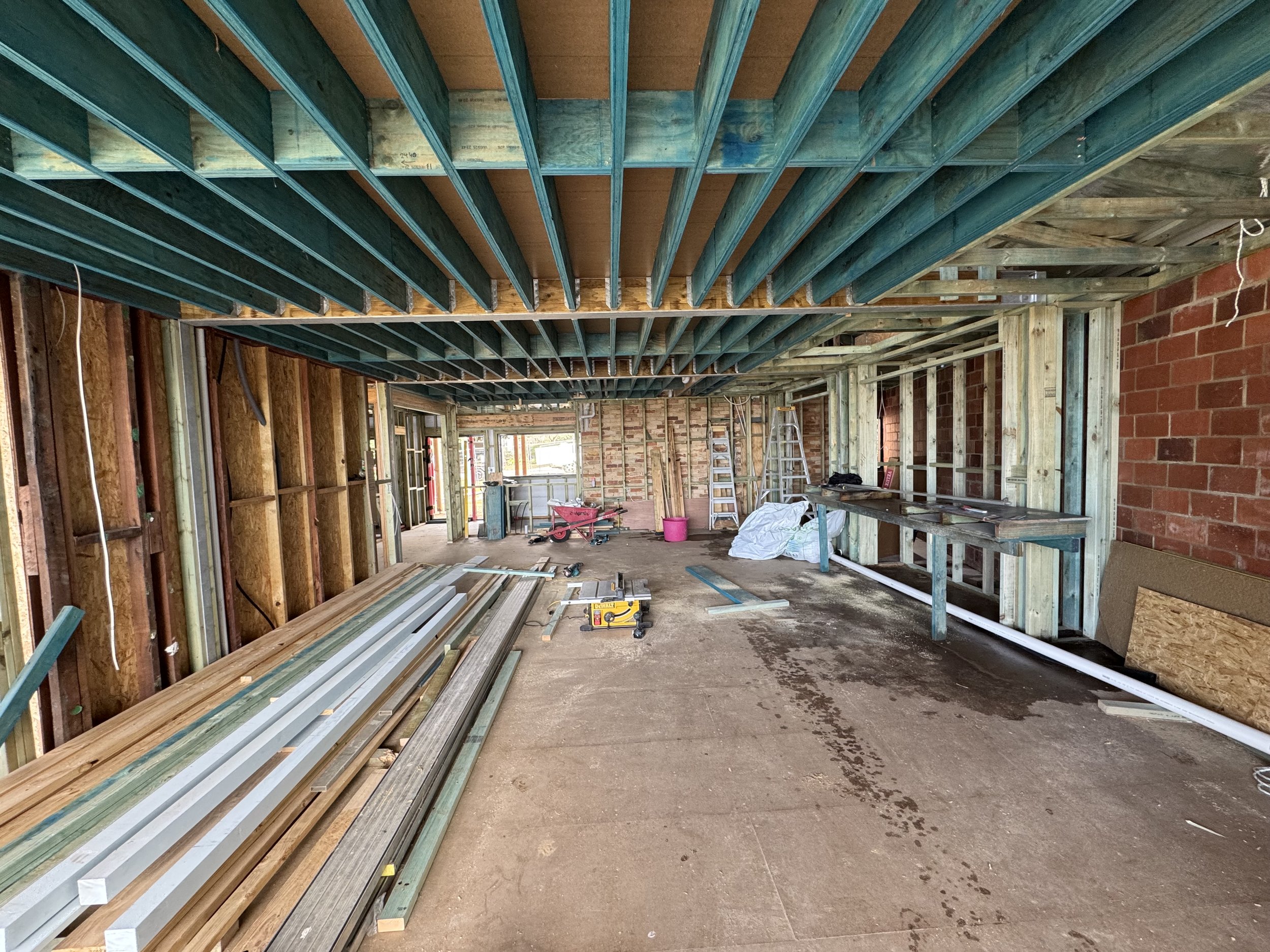 Interior of a building under construction with exposed wooden framing, metal beams, construction tools, and materials inside a partially built room.