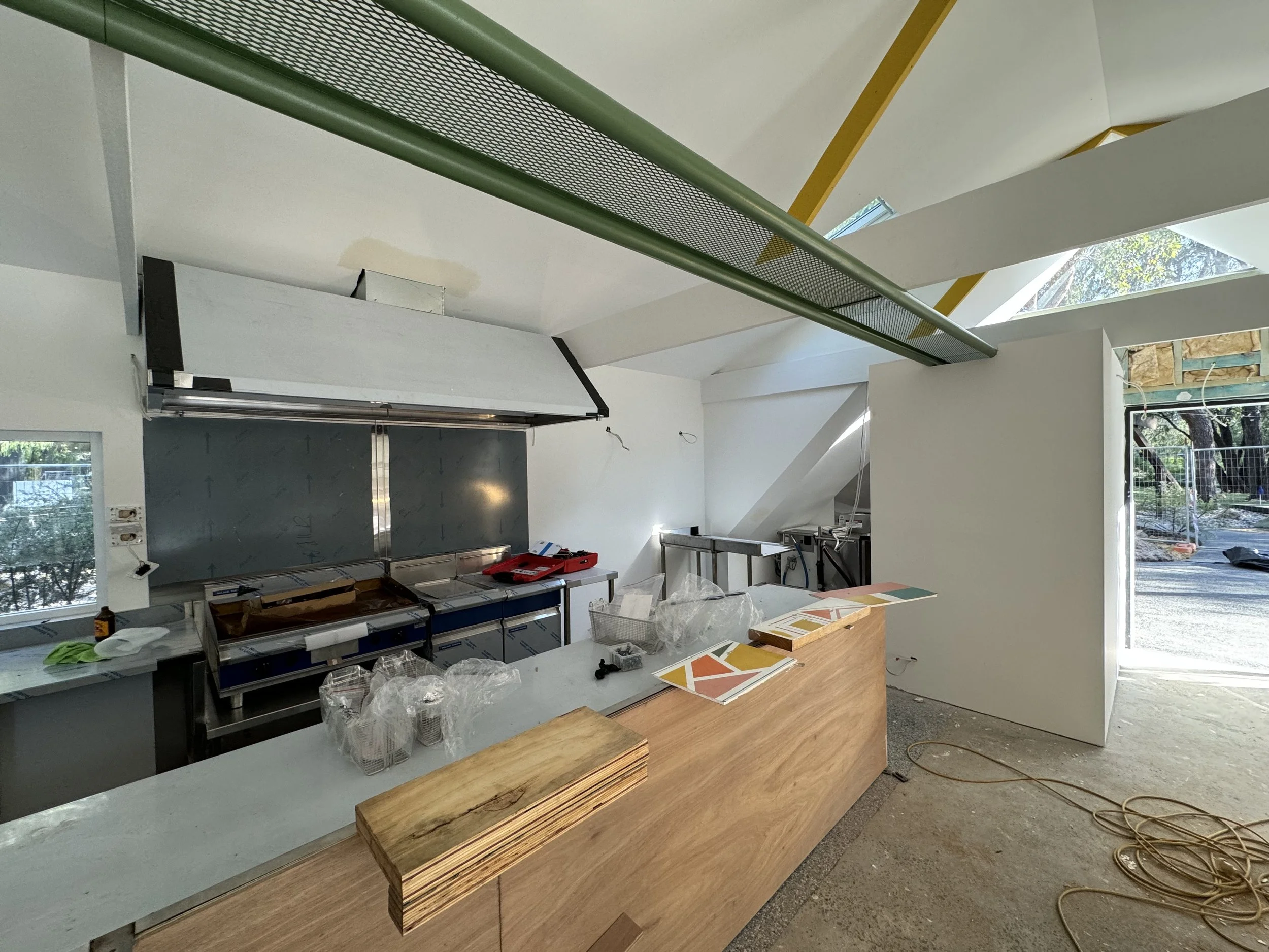 Interior view of a modern, under-construction room with a light-colored ceiling, large windows, and various construction materials and tools on a long wooden table and workbench.