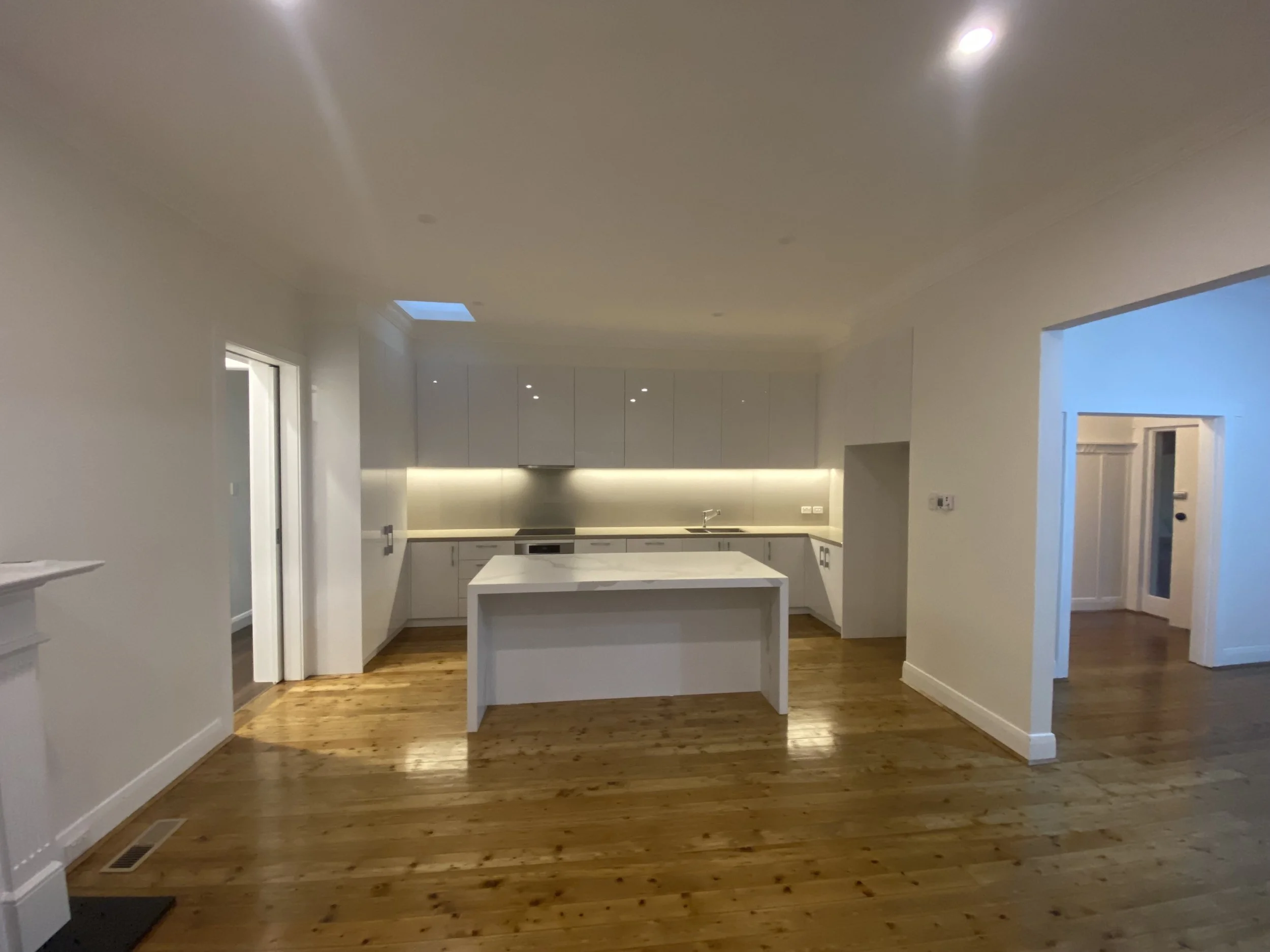 Modern kitchen with white cabinets, a marble island, and wooden flooring.