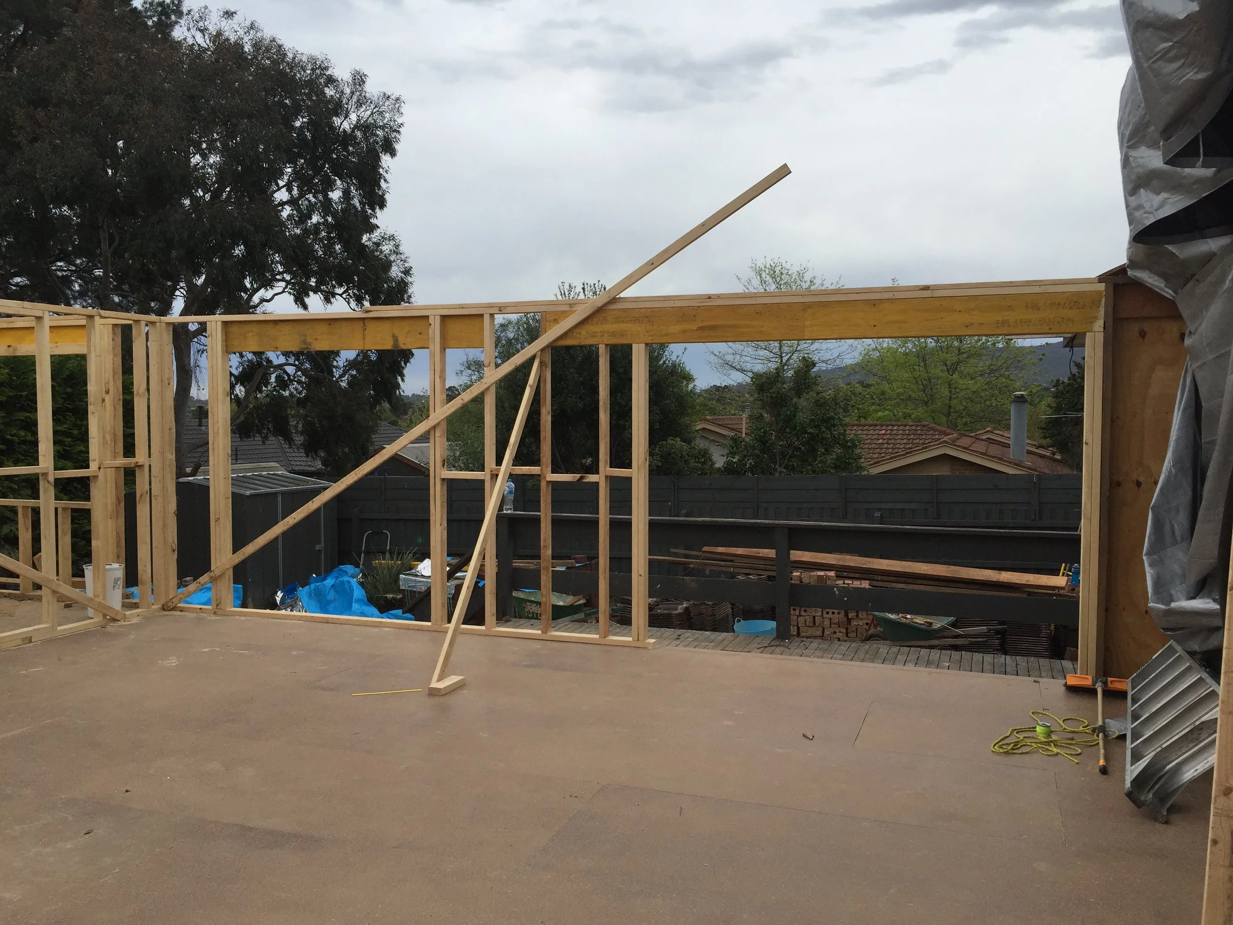 Wooden framing of a house under construction with trees and cloudy sky in the background.