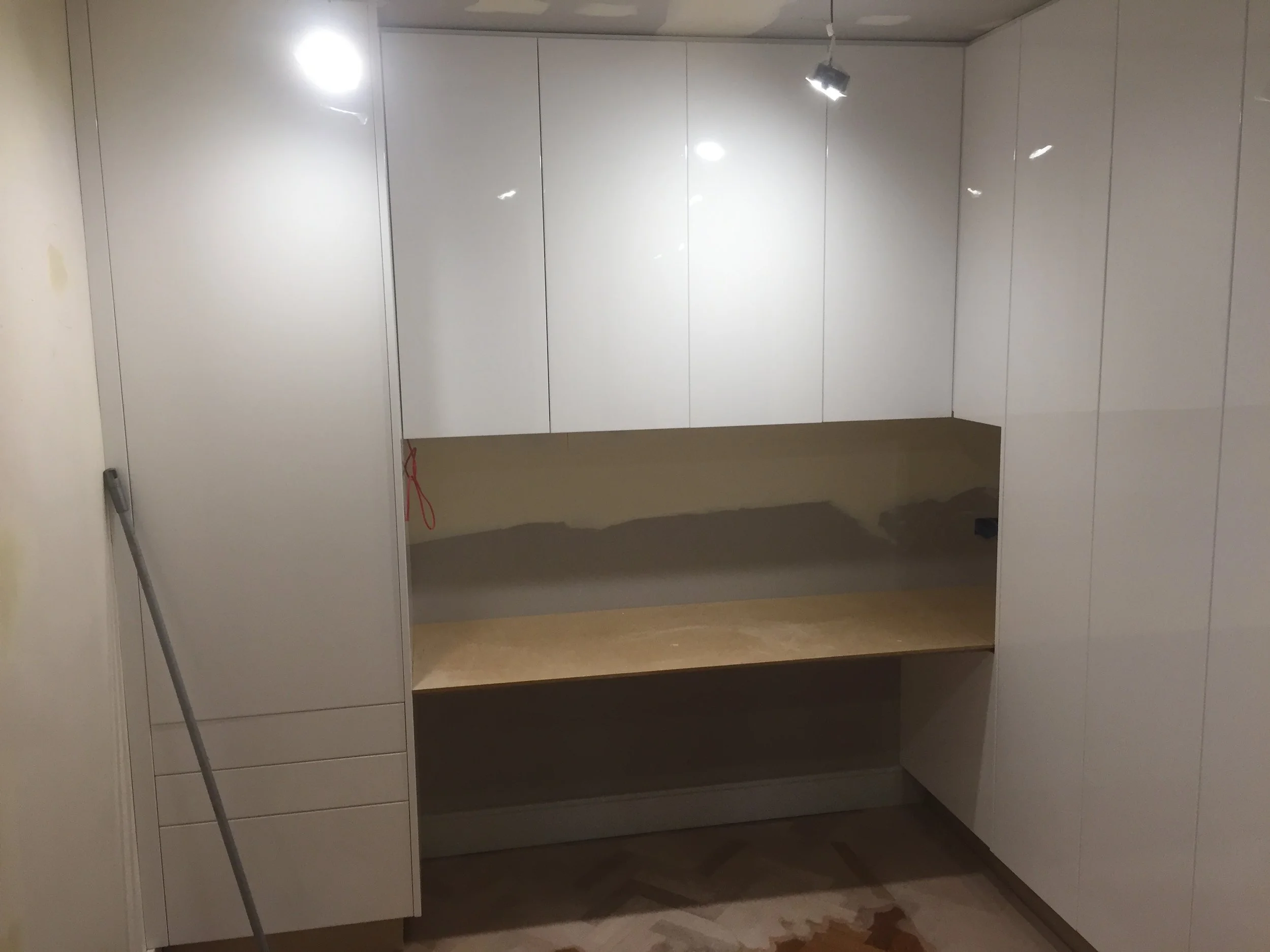 Empty white kitchen cabinet with open lower shelf, closed upper cabinets, and a gray mop leaning against the left side.