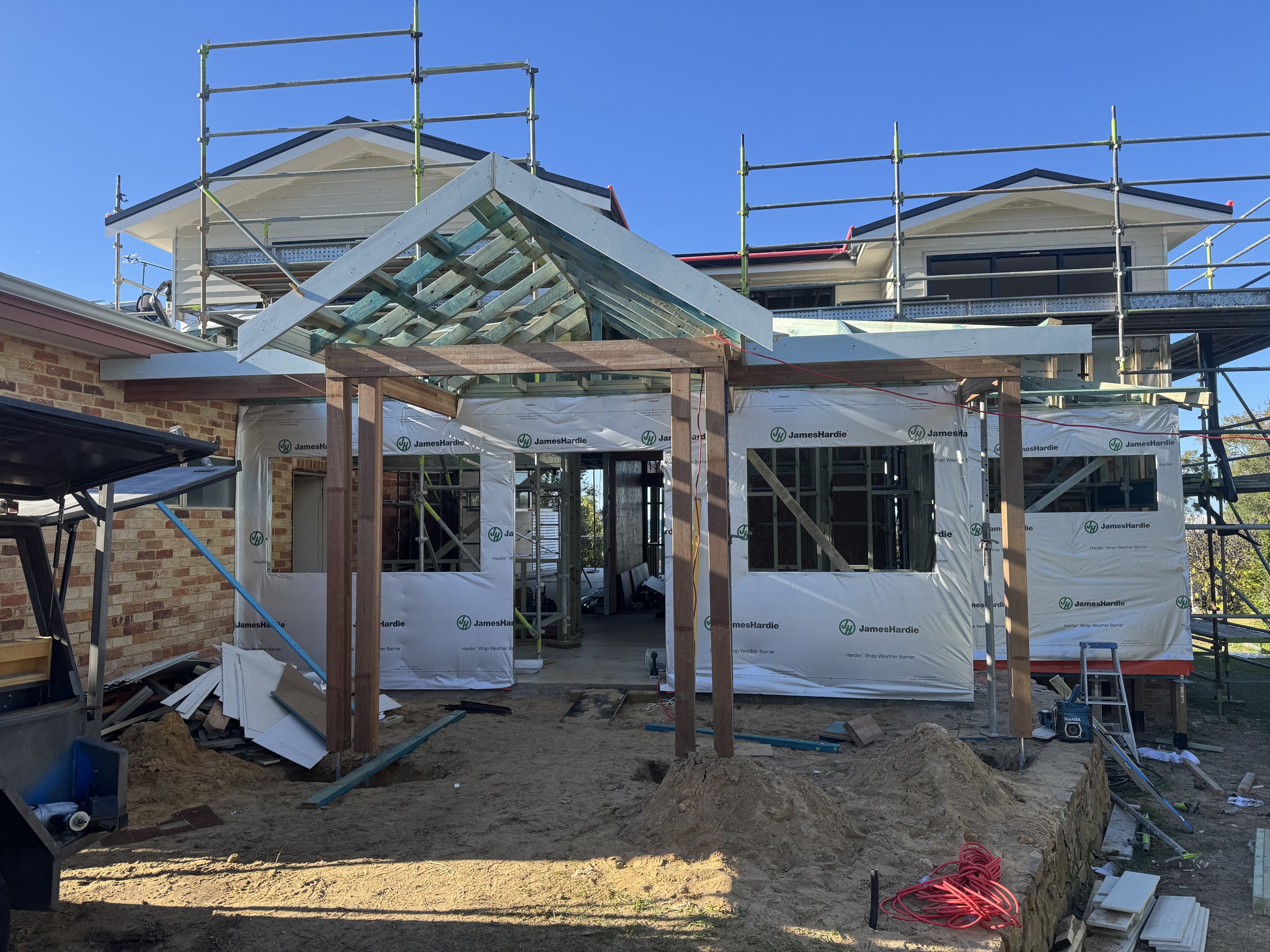 Undergoing house construction, showing scaffolding, partially built house, construction materials, and tools.