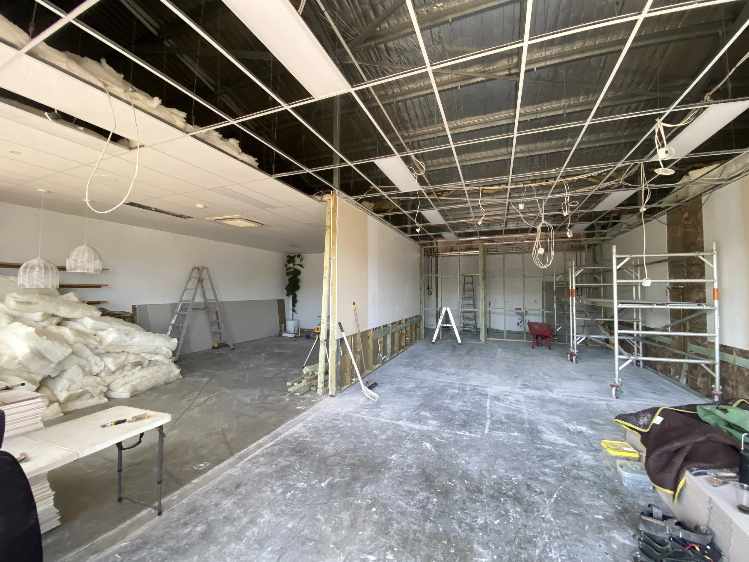 Construction site with ceiling grid installation, scaffolding, ladders, insulation, and construction tools and materials.
