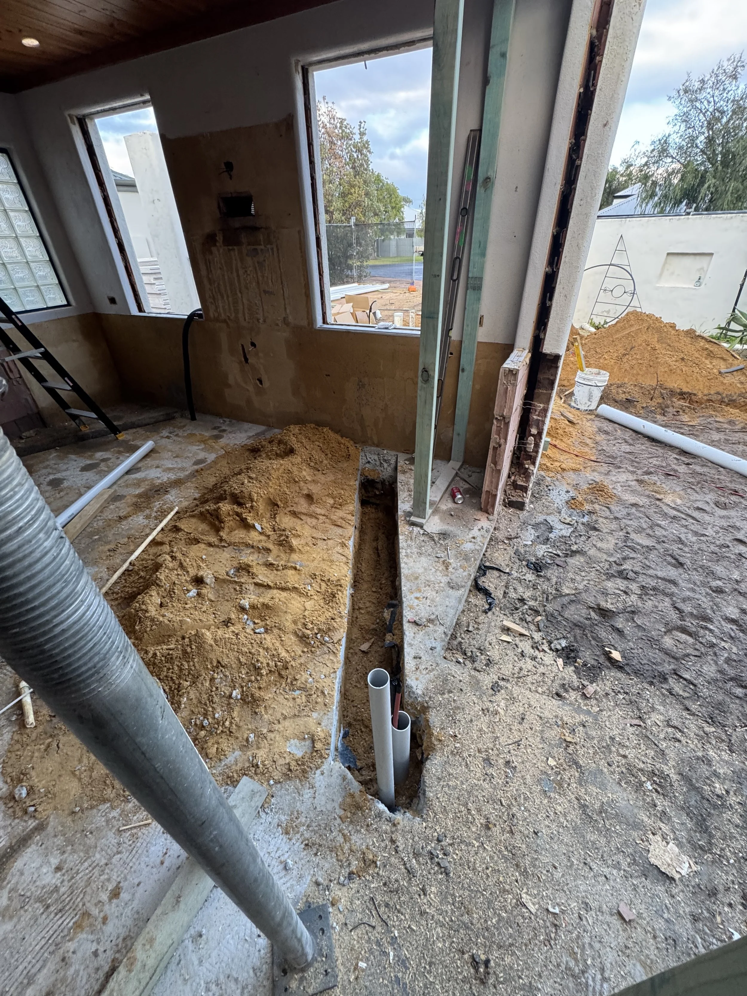 Construction site inside a house with exposed plumbing pipes, dirt, and unfinished walls, during building or remodeling.