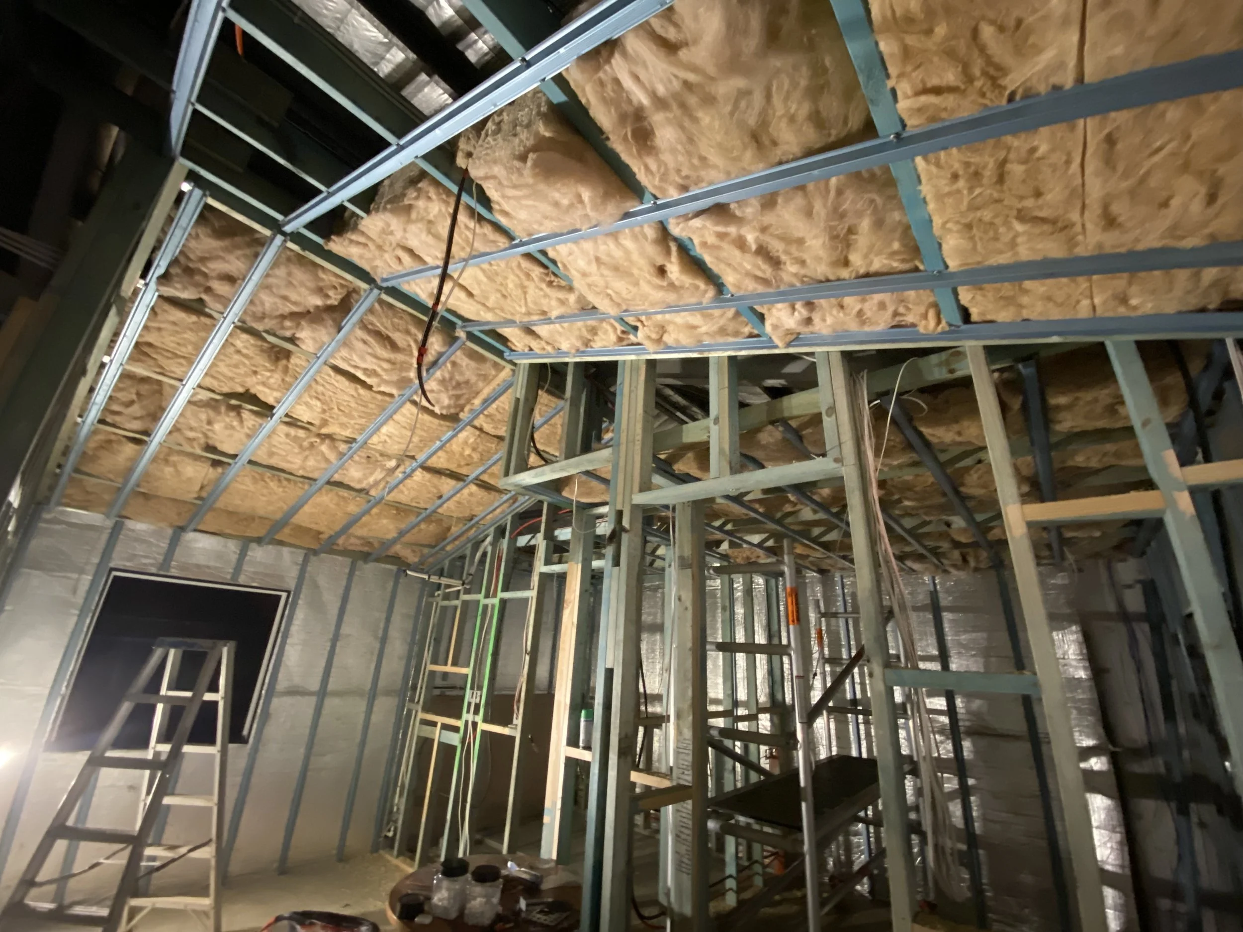 Construction site with metal framing and yellow insulation material installed in the ceiling area.