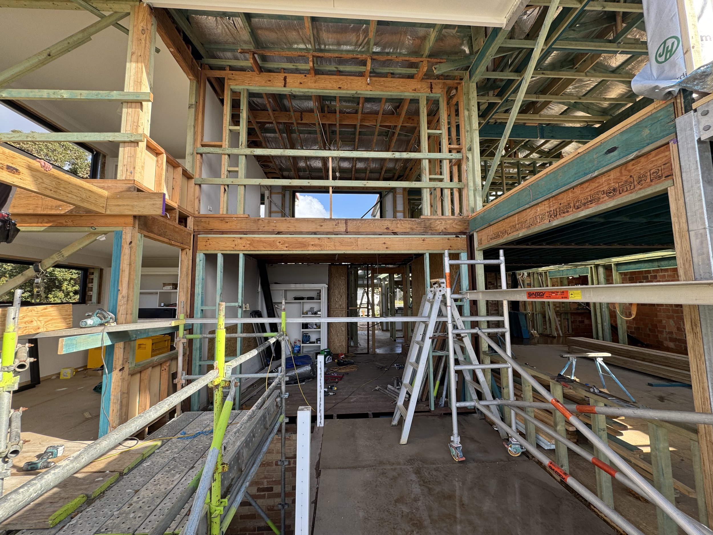Construction site of a multi-story building showing wooden framing, scaffolding, and partially completed walls with some interior spaces visible.