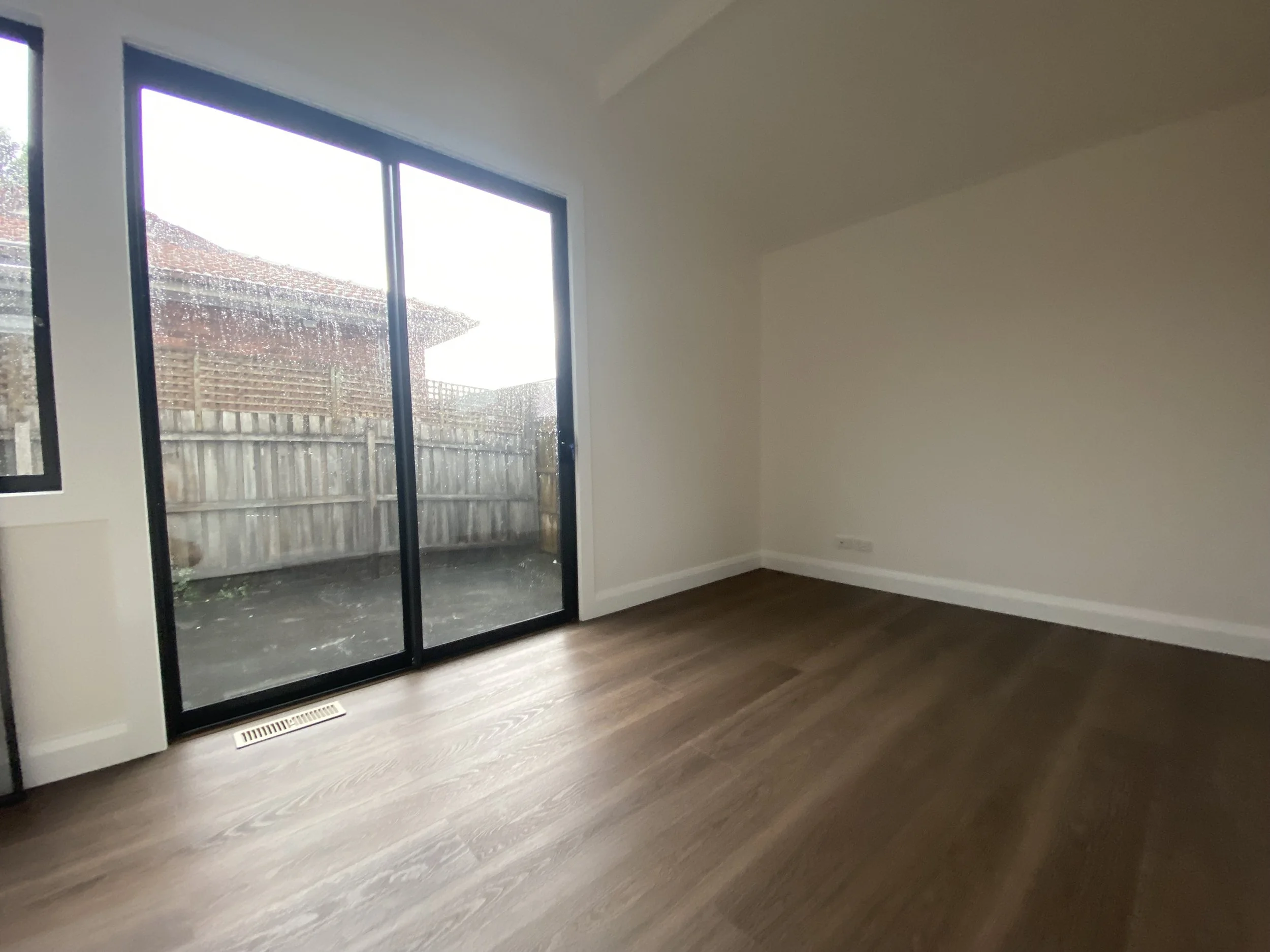 Empty room with large sliding glass door leading to backyard, hardwood floors, and white walls.