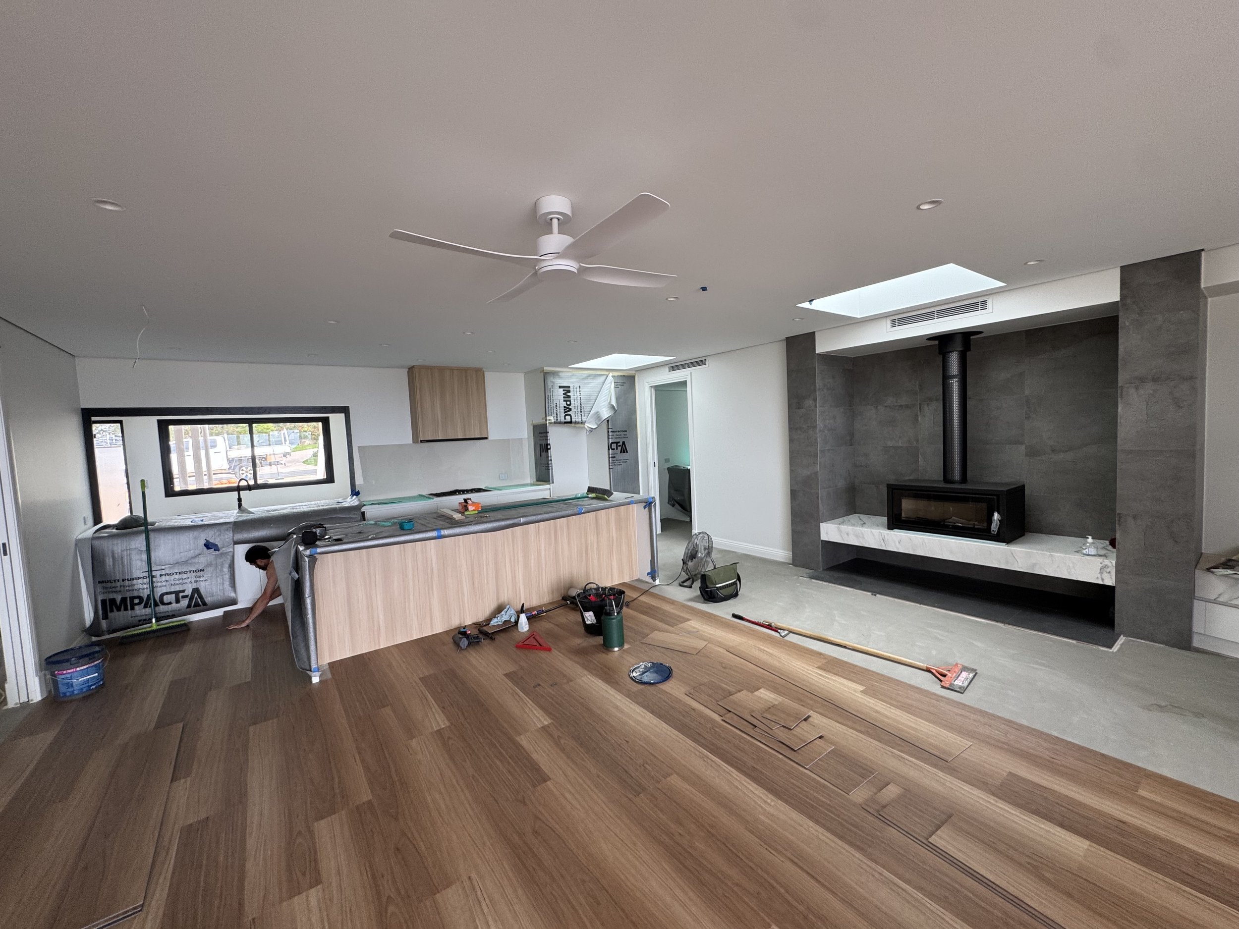 Living room under renovation with hardwood floors, a white ceiling fan, a fireplace, and construction tools and materials scattered around.