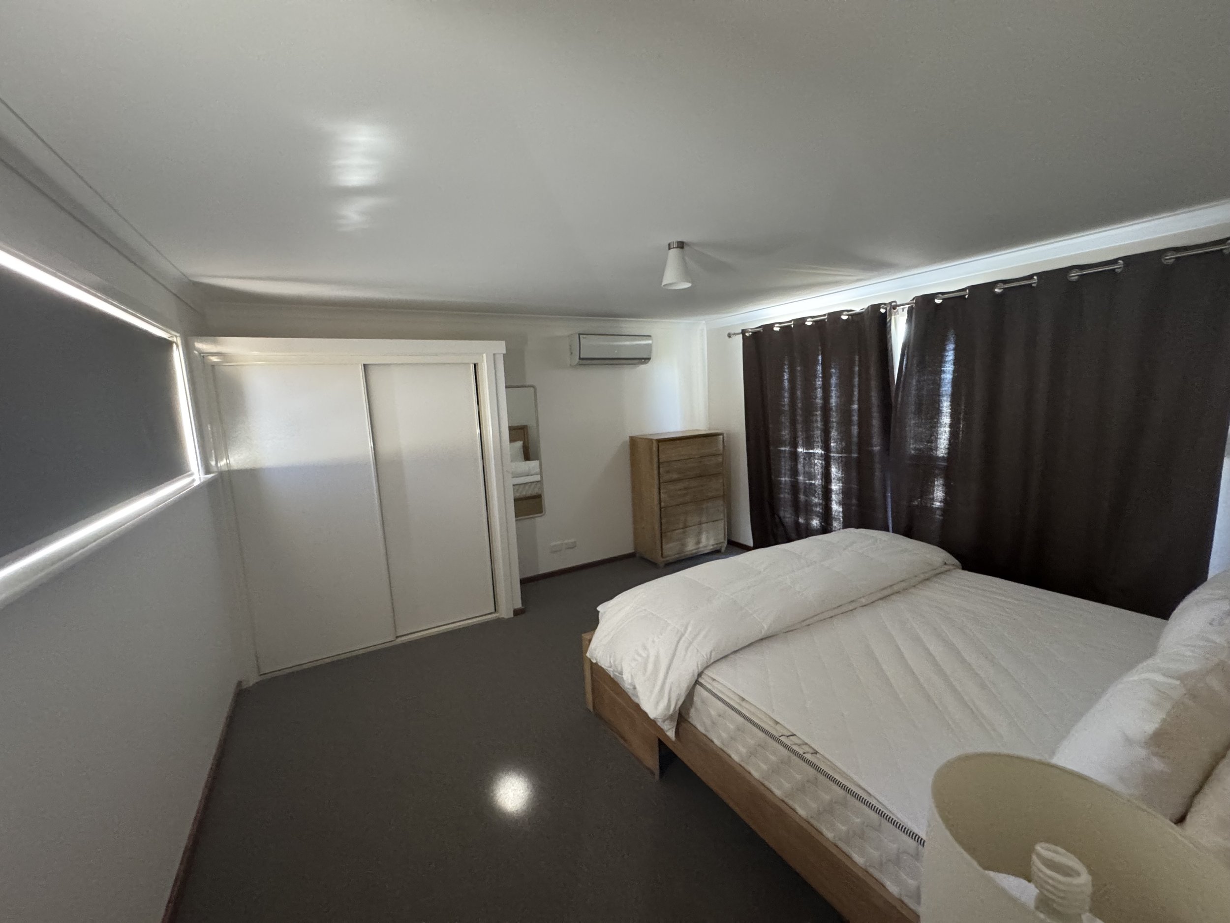 A bedroom with a bed, dark curtains, a window, and an air conditioning unit on the wall.