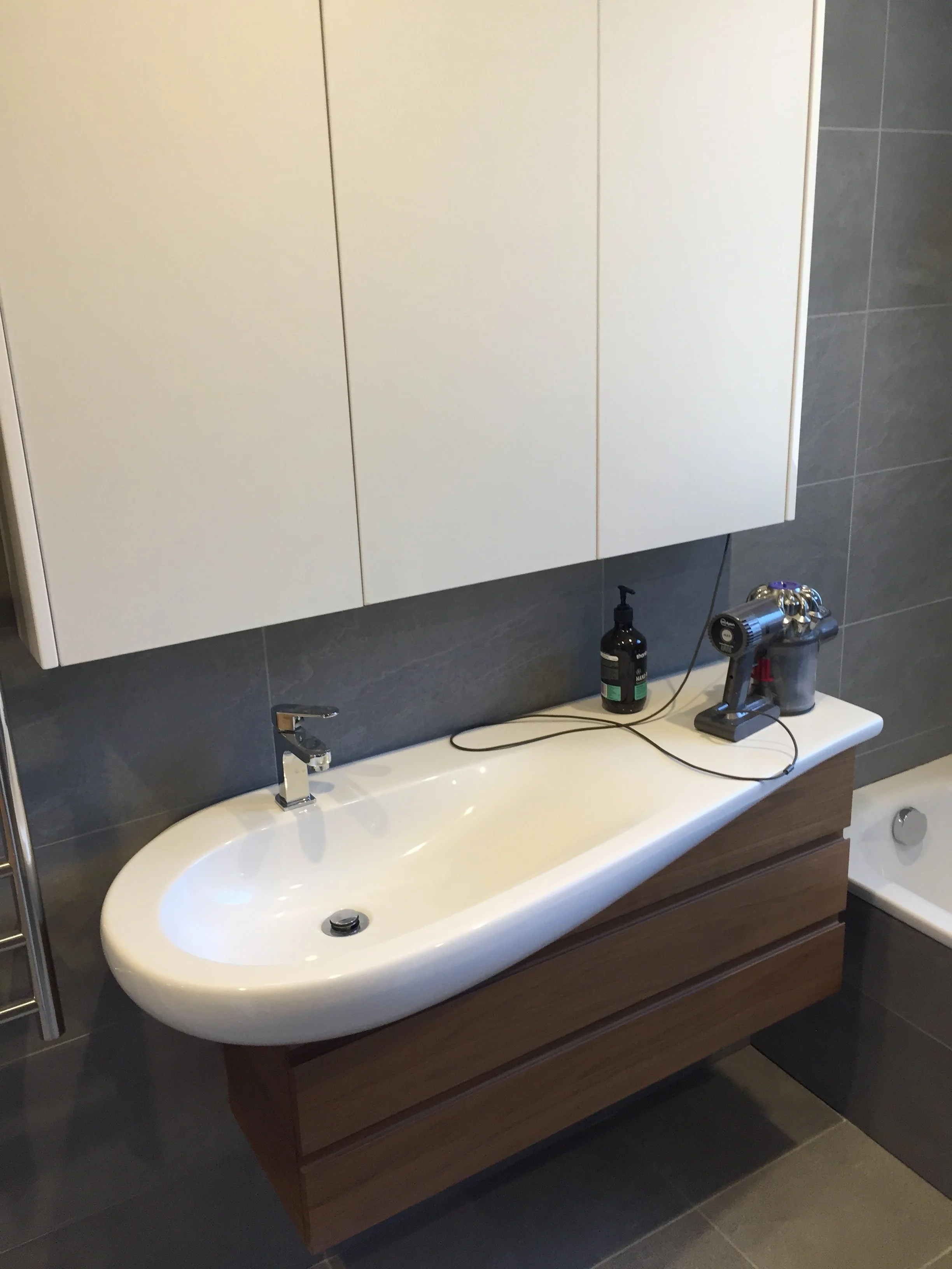 Bathroom sink with a wooden cabinet, a mirror cabinet above, and items including a soap dispenser and a tool on the sink.